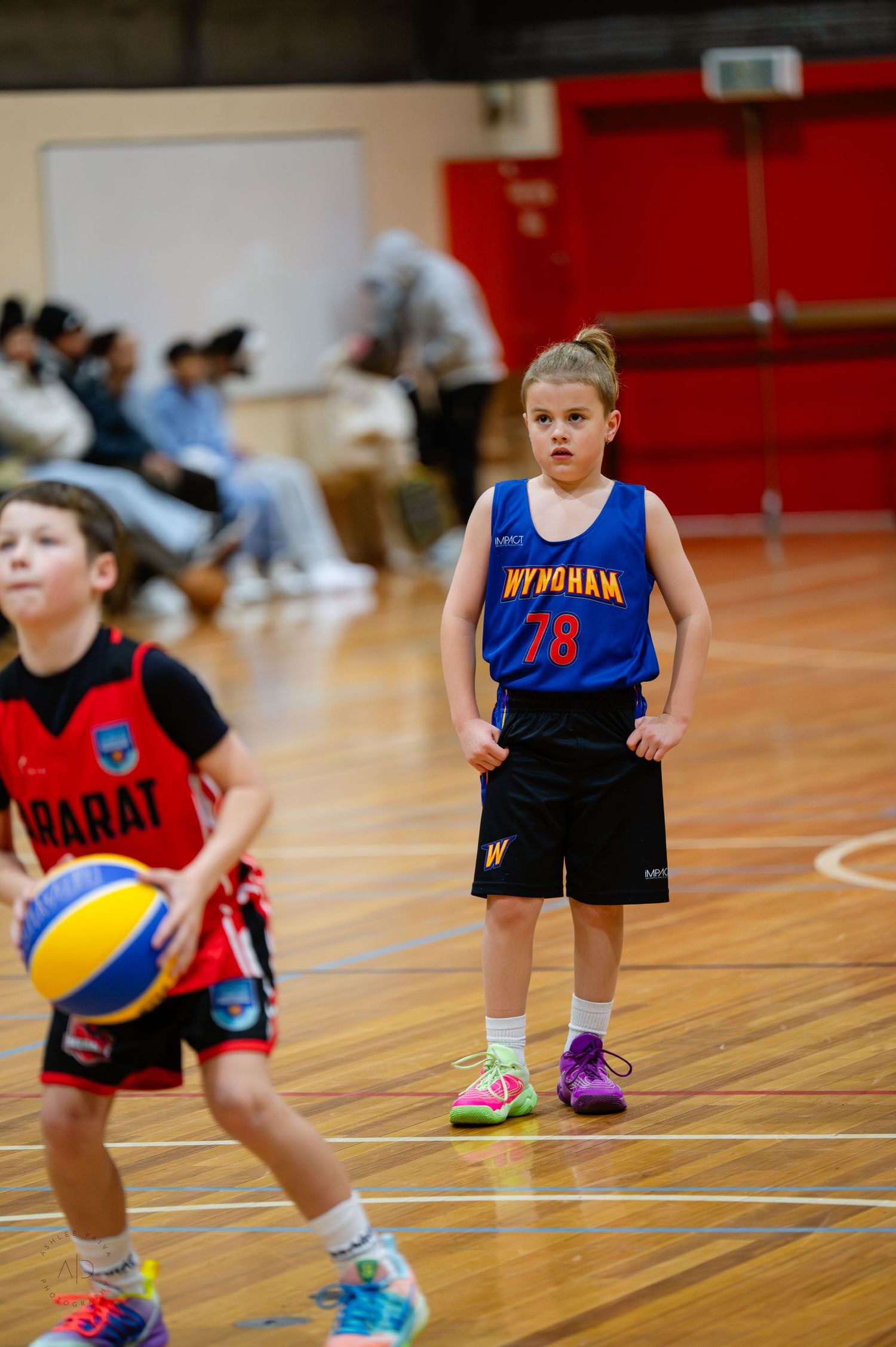 Two young children playing basketball in a gymnasium, wearing Wyndham and Barat team uniforms during a youth basketball game.