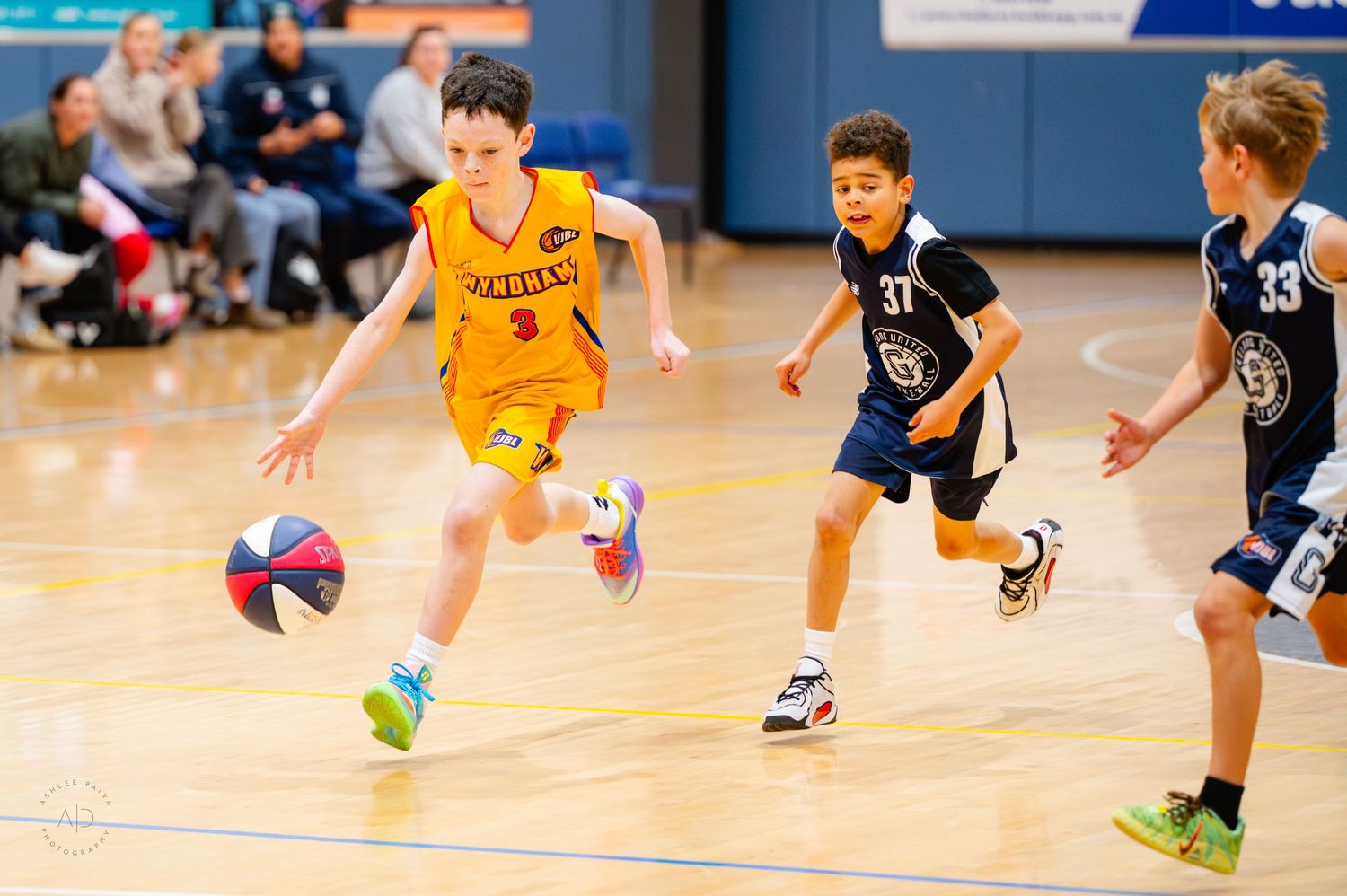 Young boy in yellow jersey dribbling basketball during youth league game, defenders in navy uniforms chasing.