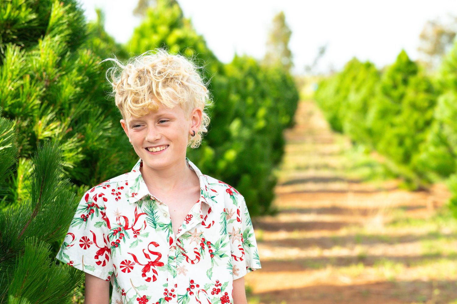 Family members pose in matching floral prints along a row of evergreen trees.