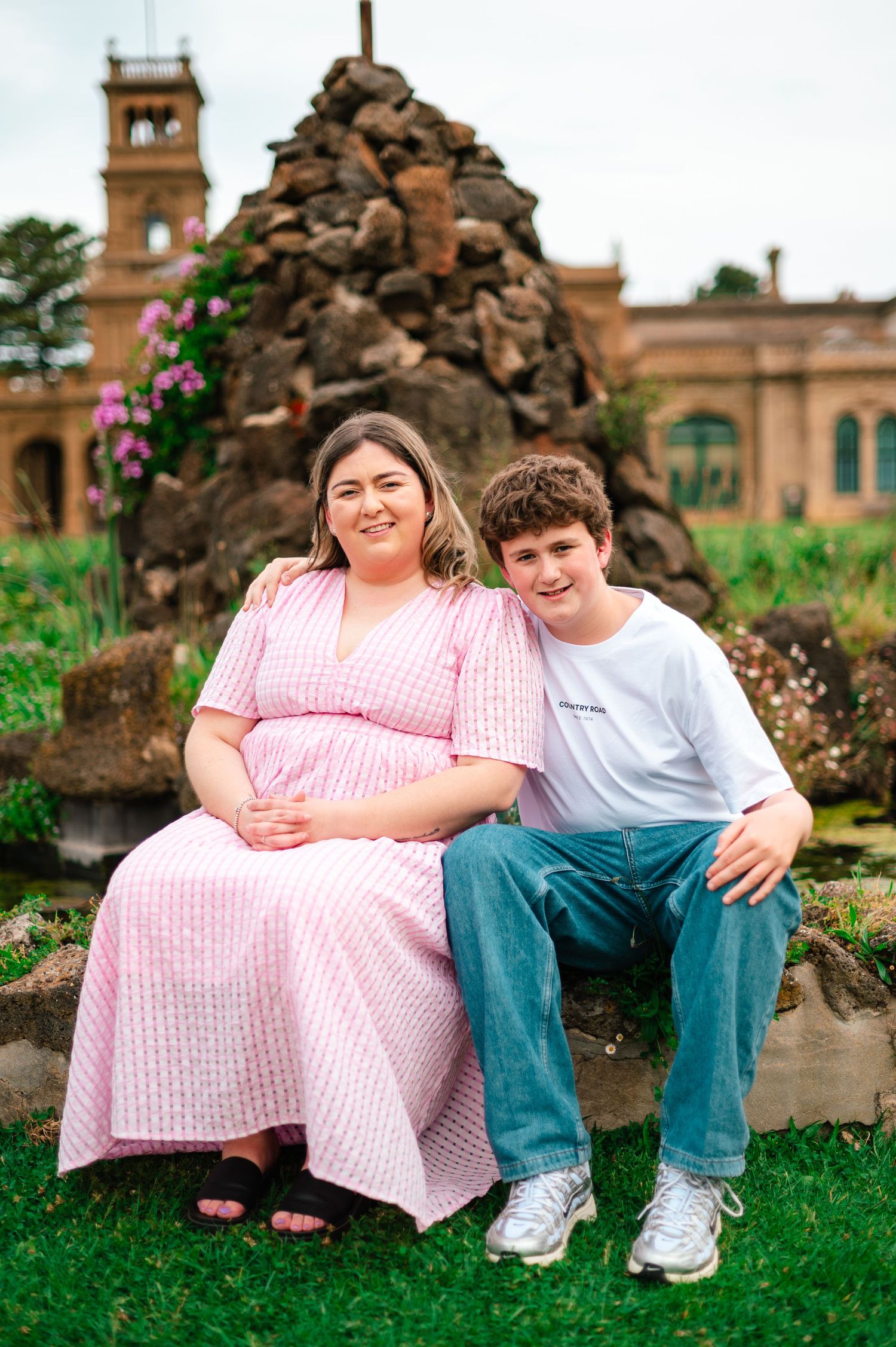 Two people sitting together on stone steps near a historic brick building with gardens.