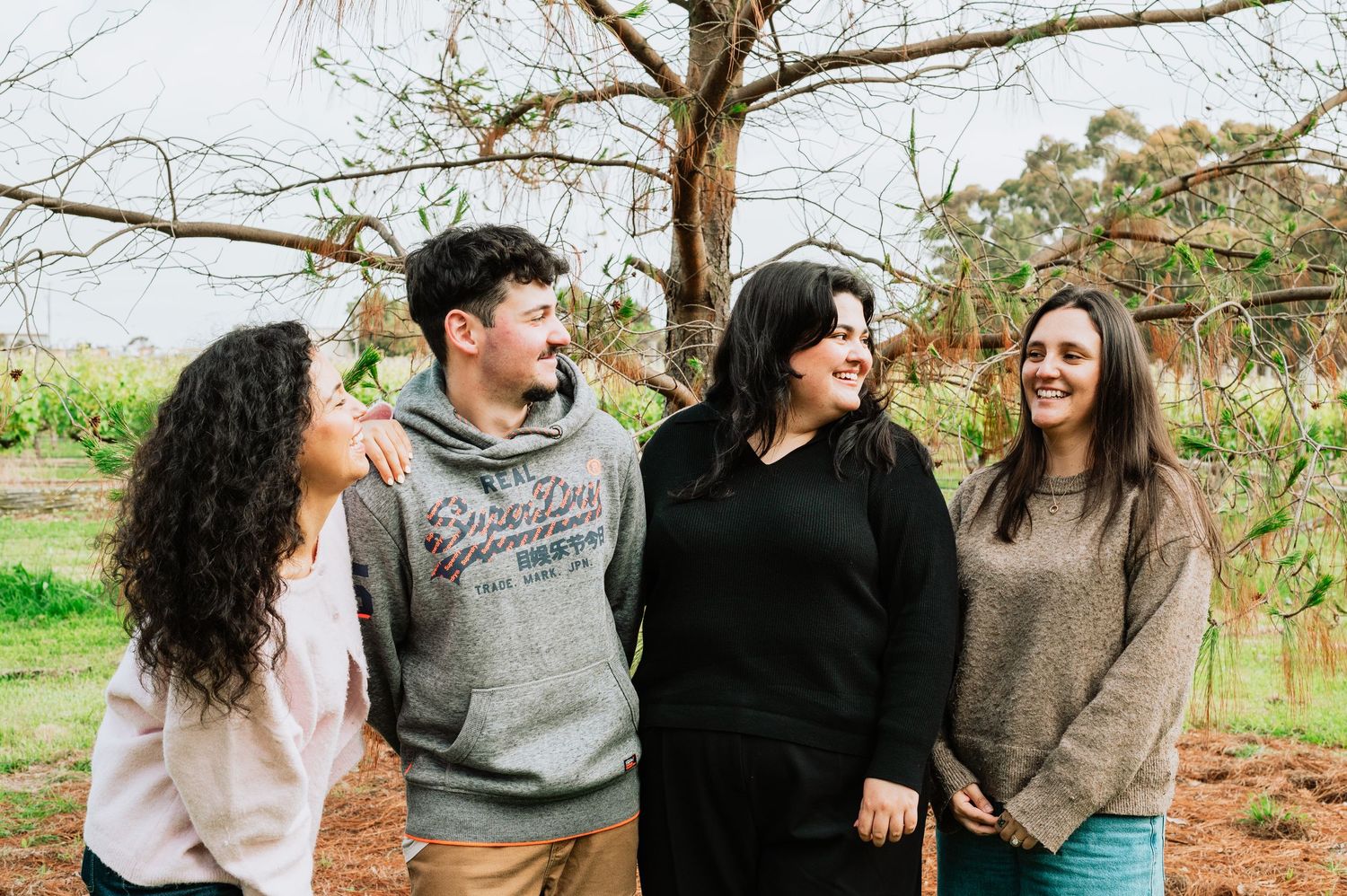 A joyful group poses together outdoors in casual attire against a natural background.
