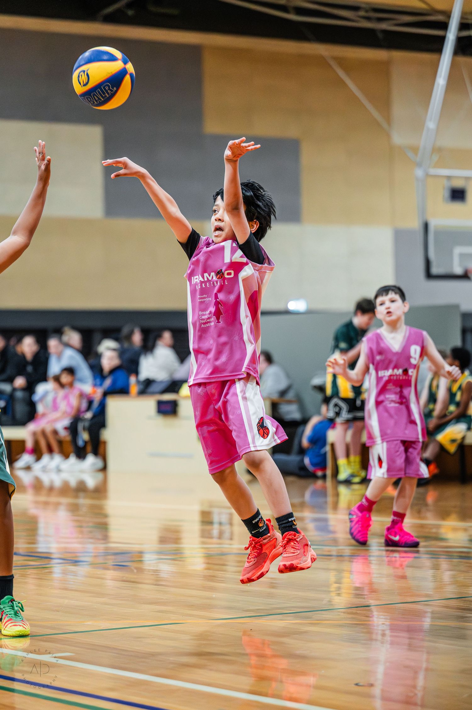 Young basketball player in pink uniform jumps to shoot ball during indoor youth basketball game.