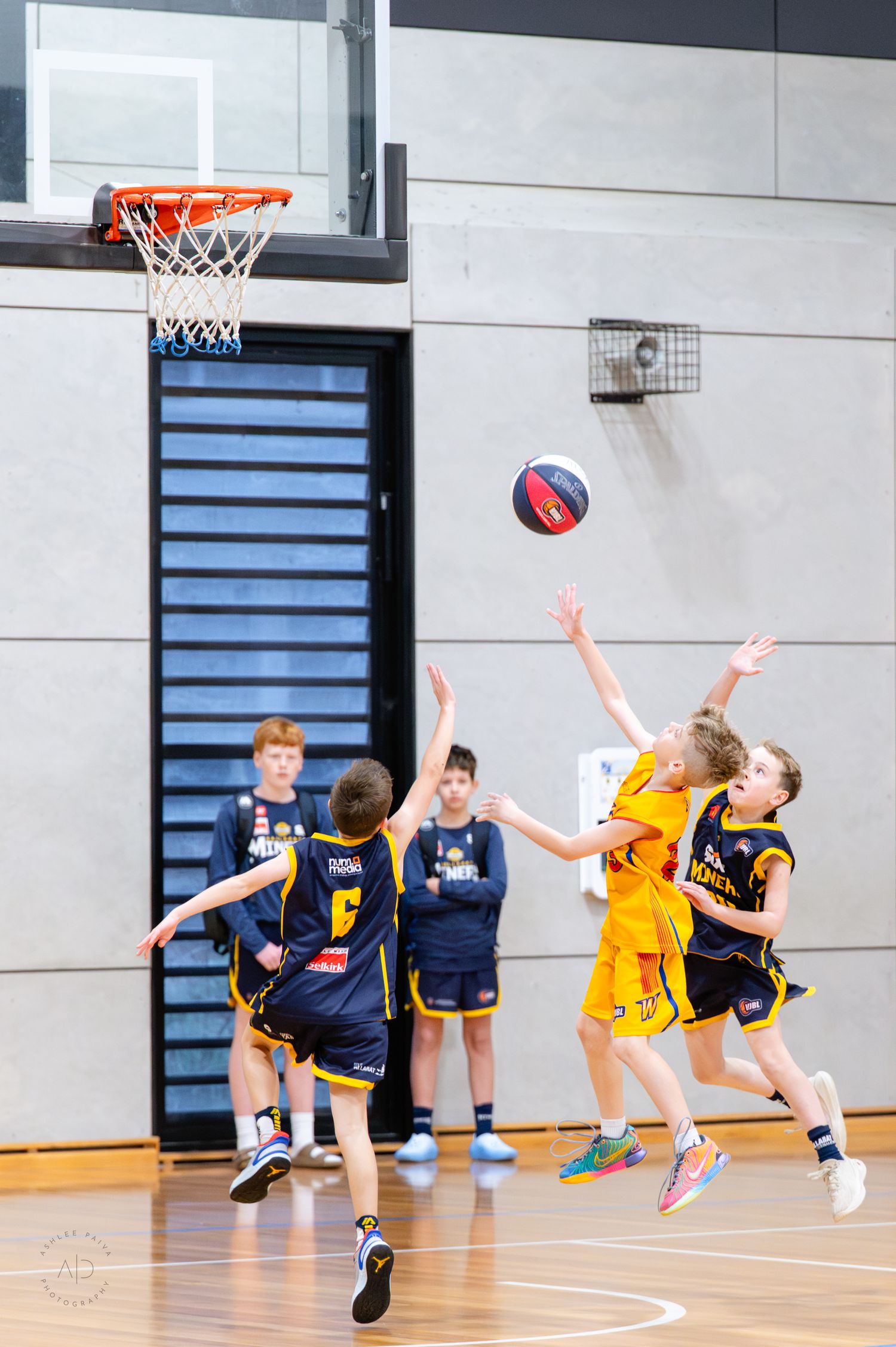 Young boys playing indoor basketball game, player in yellow jumping to shoot ball near the hoop during youth league match.