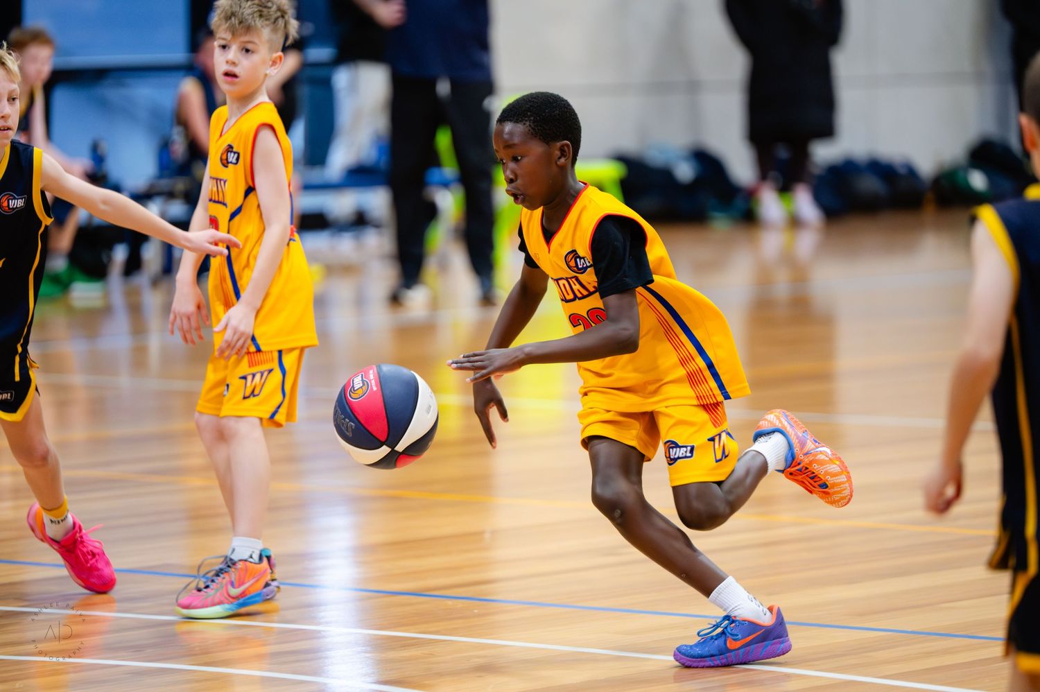 Young basketball players in yellow uniforms compete in an indoor youth basketball game, with one player dribbling the ball.