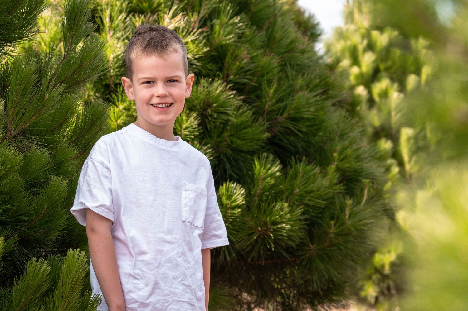 Candid outdoor portrait with green pine trees creating natural backdrop.