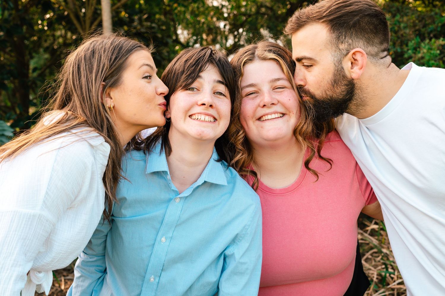 Family wearing coordinated blue and pink outfits poses together outdoors in a natural setting.