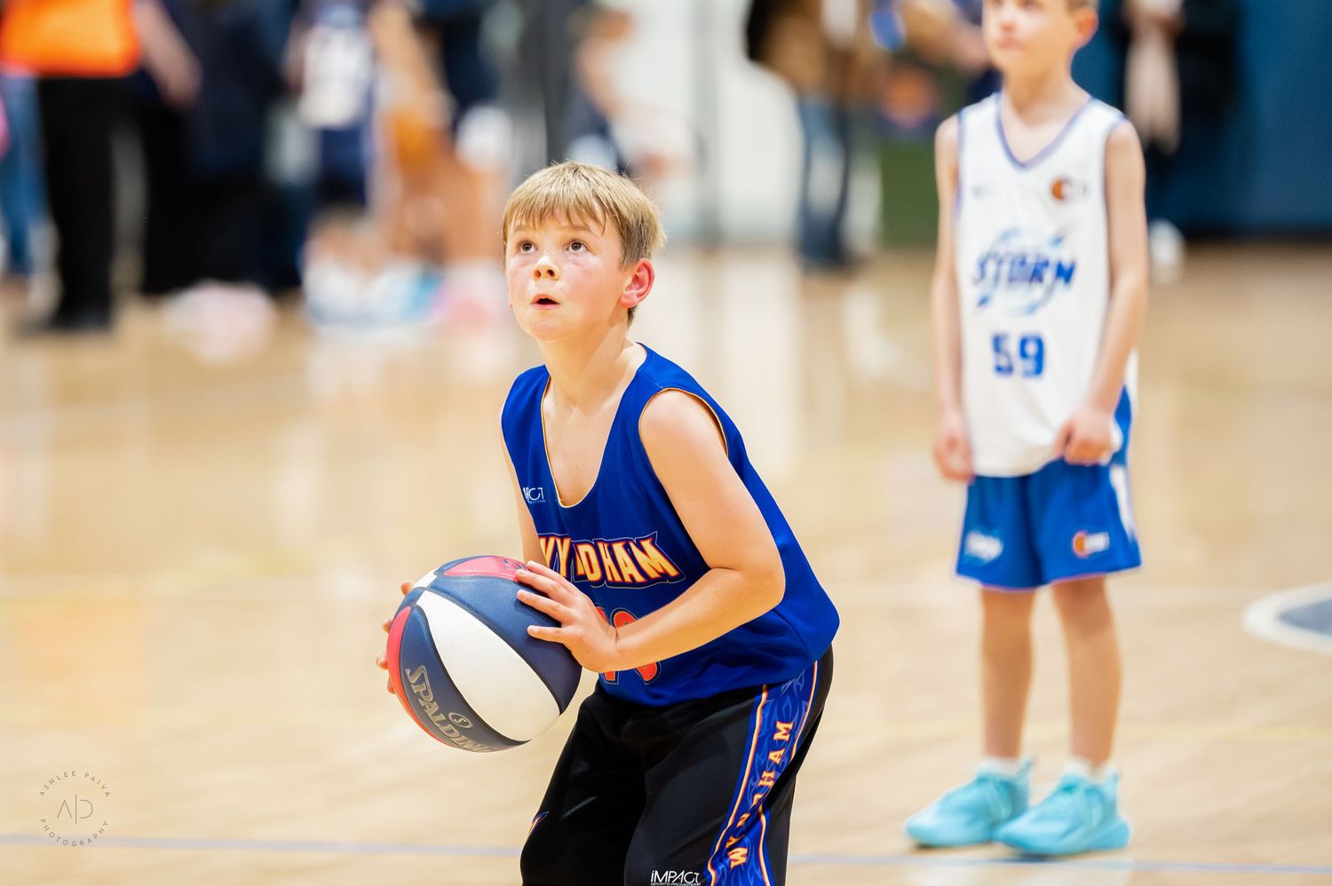 Young boy in blue basketball uniform dribbling ball on indoor court during youth basketball game.