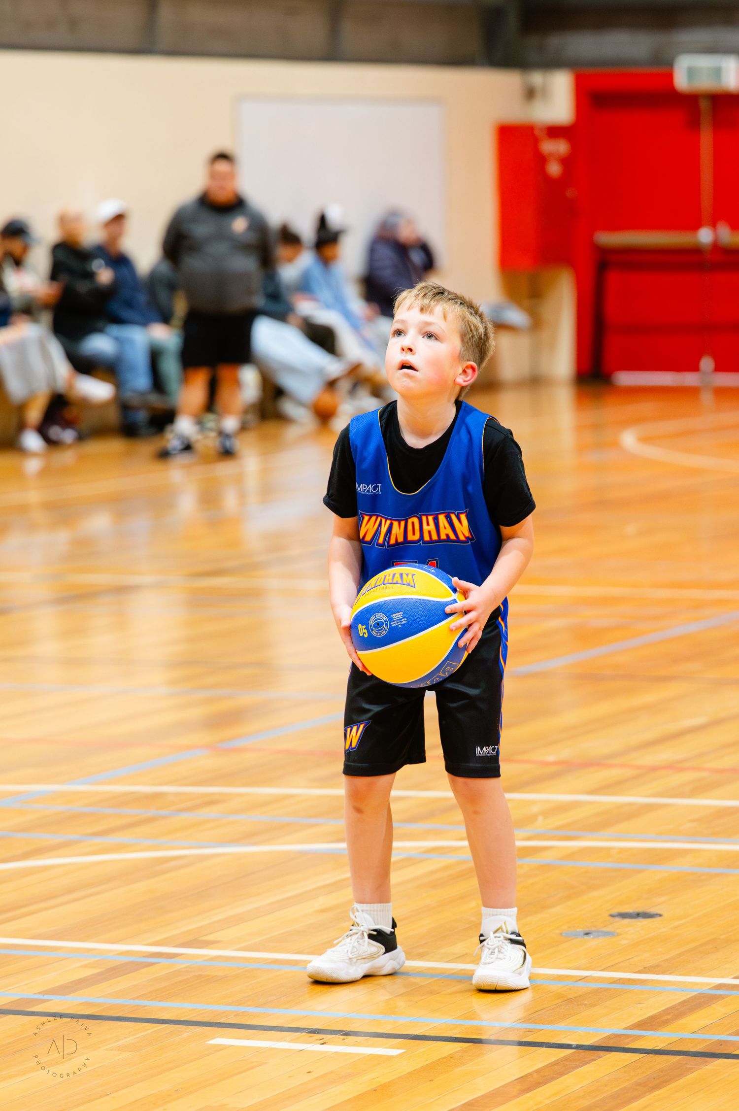 Young boy in Wyndham basketball uniform holding a ball on an indoor court during a youth basketball game.