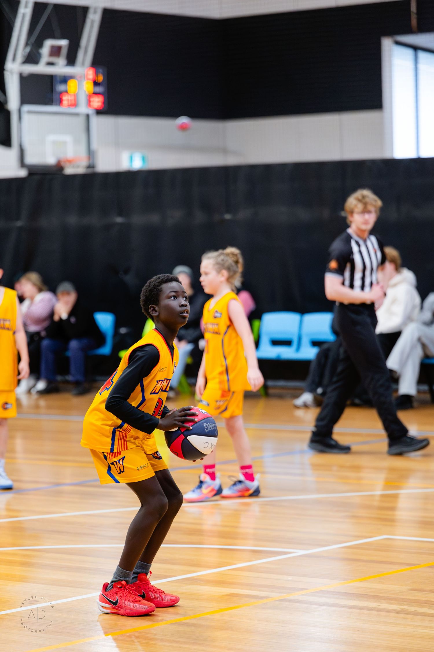 Young basketball player in yellow uniform prepares to shoot during an indoor youth basketball game.