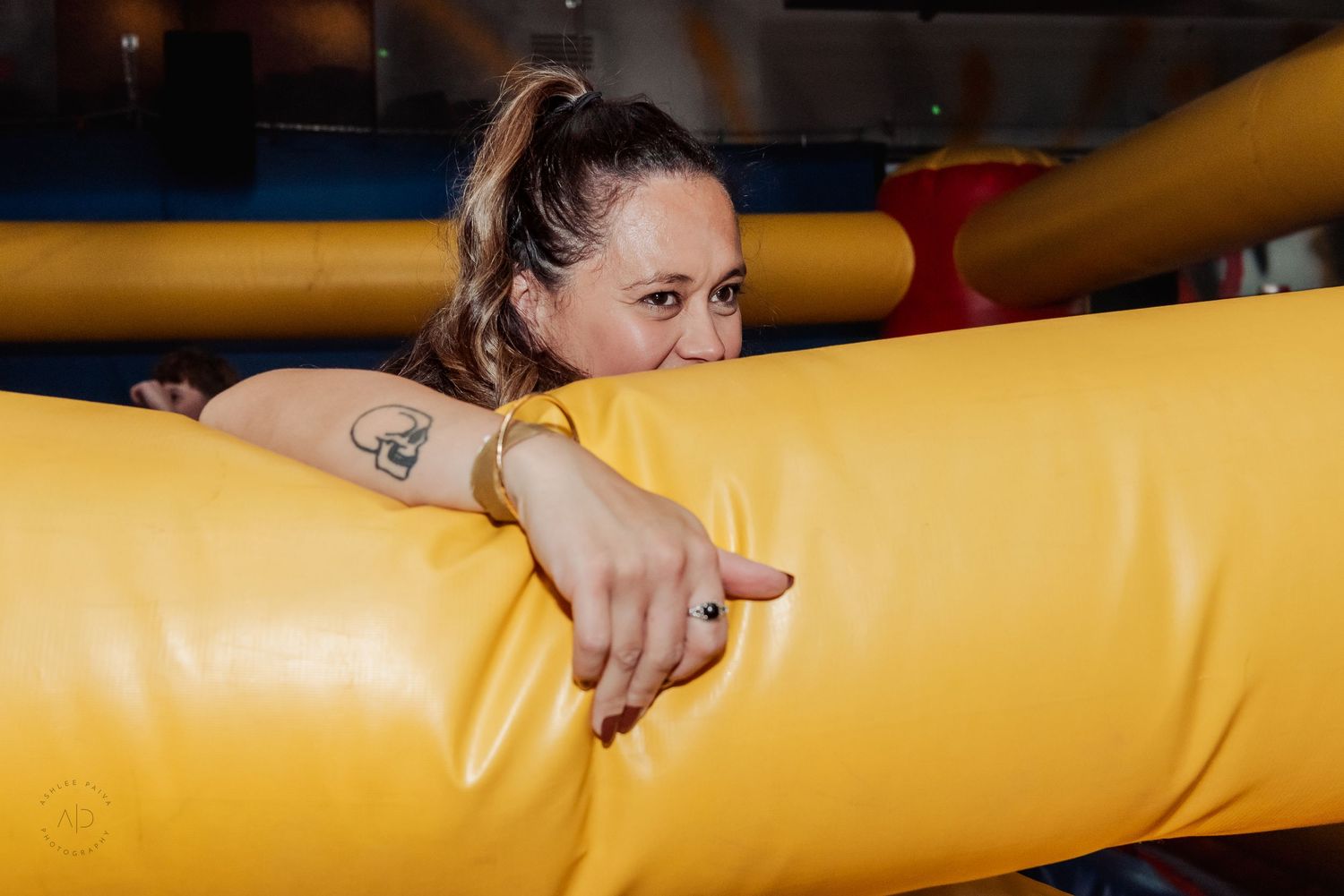 Woman smiling and hugging a large yellow inflatable obstacle at an indoor play center.