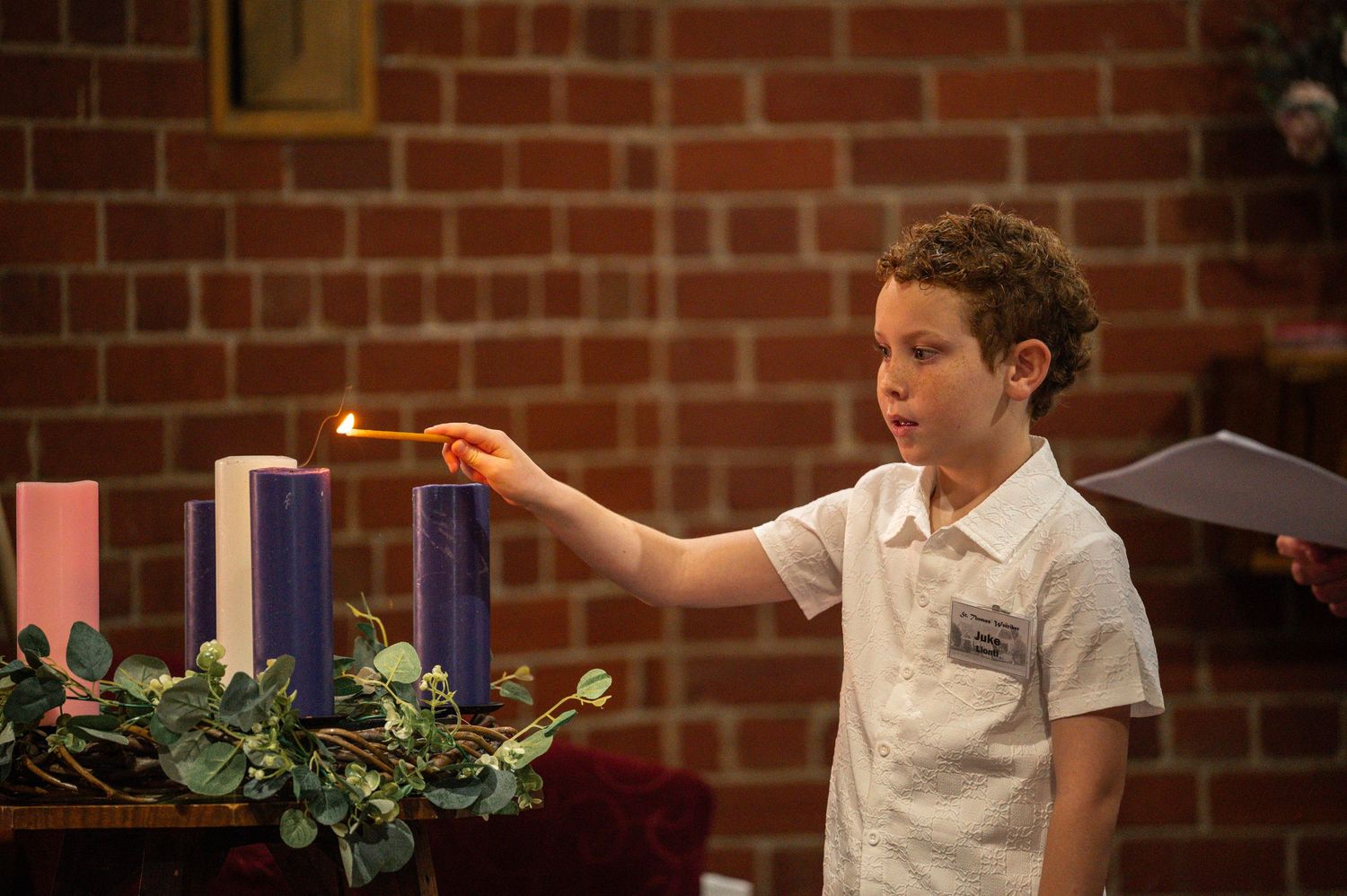 A child in white clothing lights advent candles at a church ceremony.