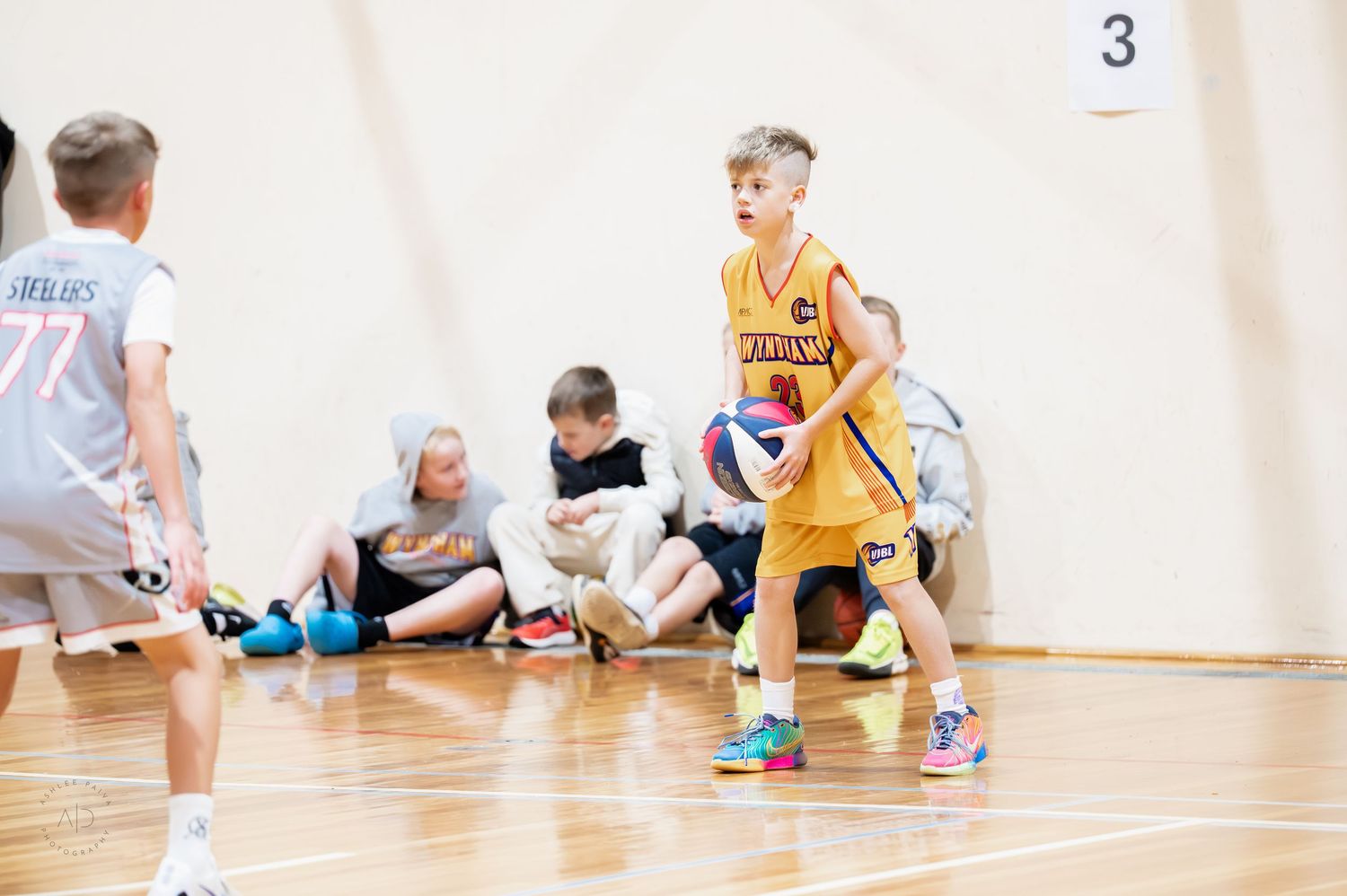 Young boy in yellow jersey dribbling basketball during indoor youth basketball game with teammates on court.