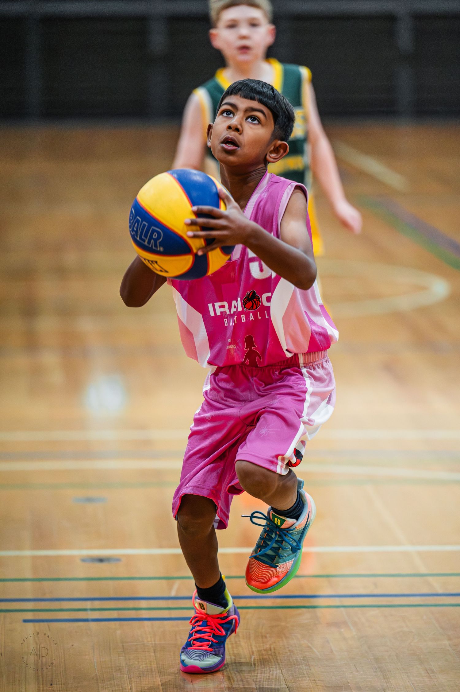 Young boy in pink uniform dribbling basketball on indoor court during youth league game.