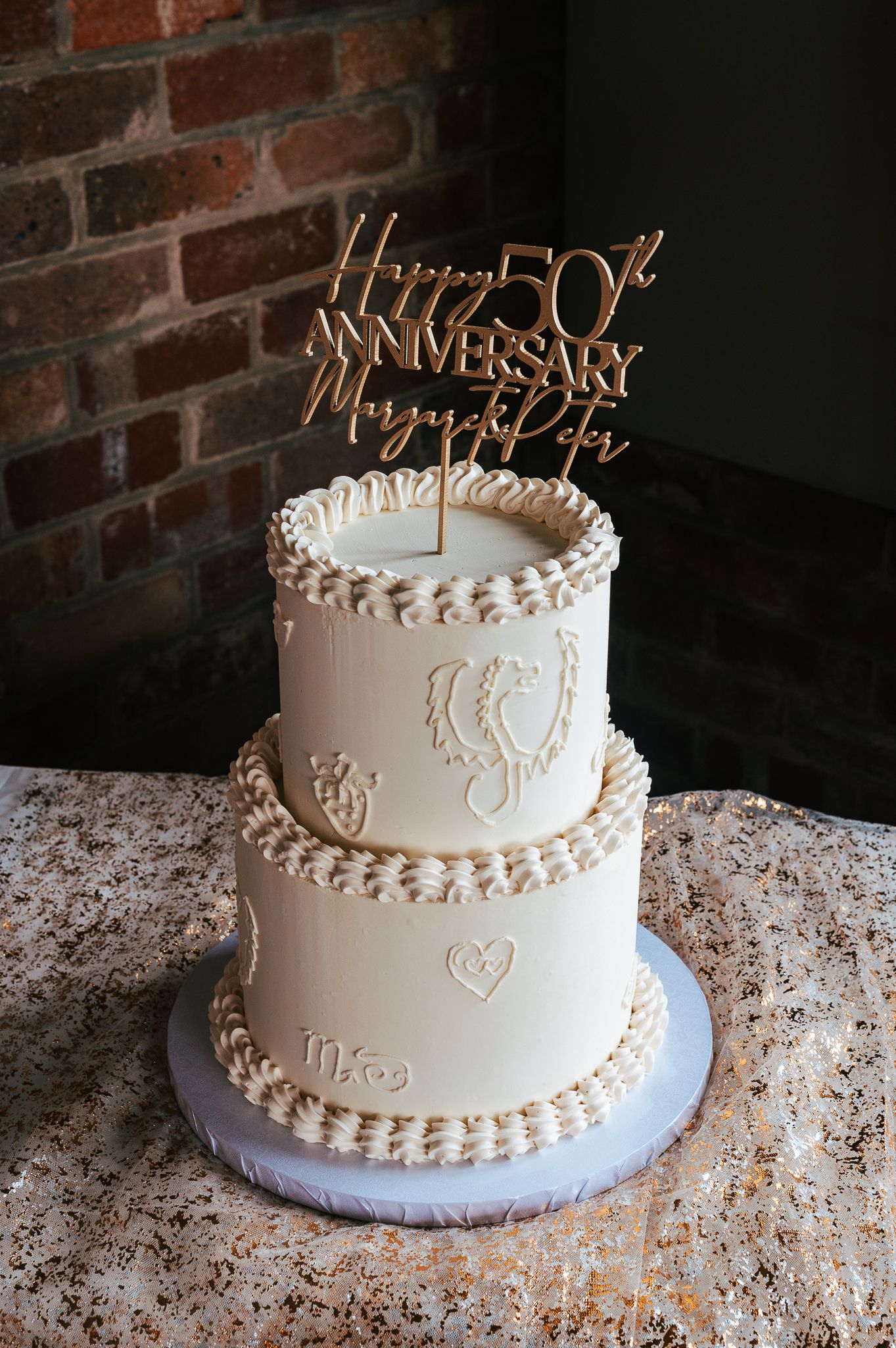 Elegant two-tier white anniversary cake with gold topper and delicate piped details celebrating 50 years of marriage.
