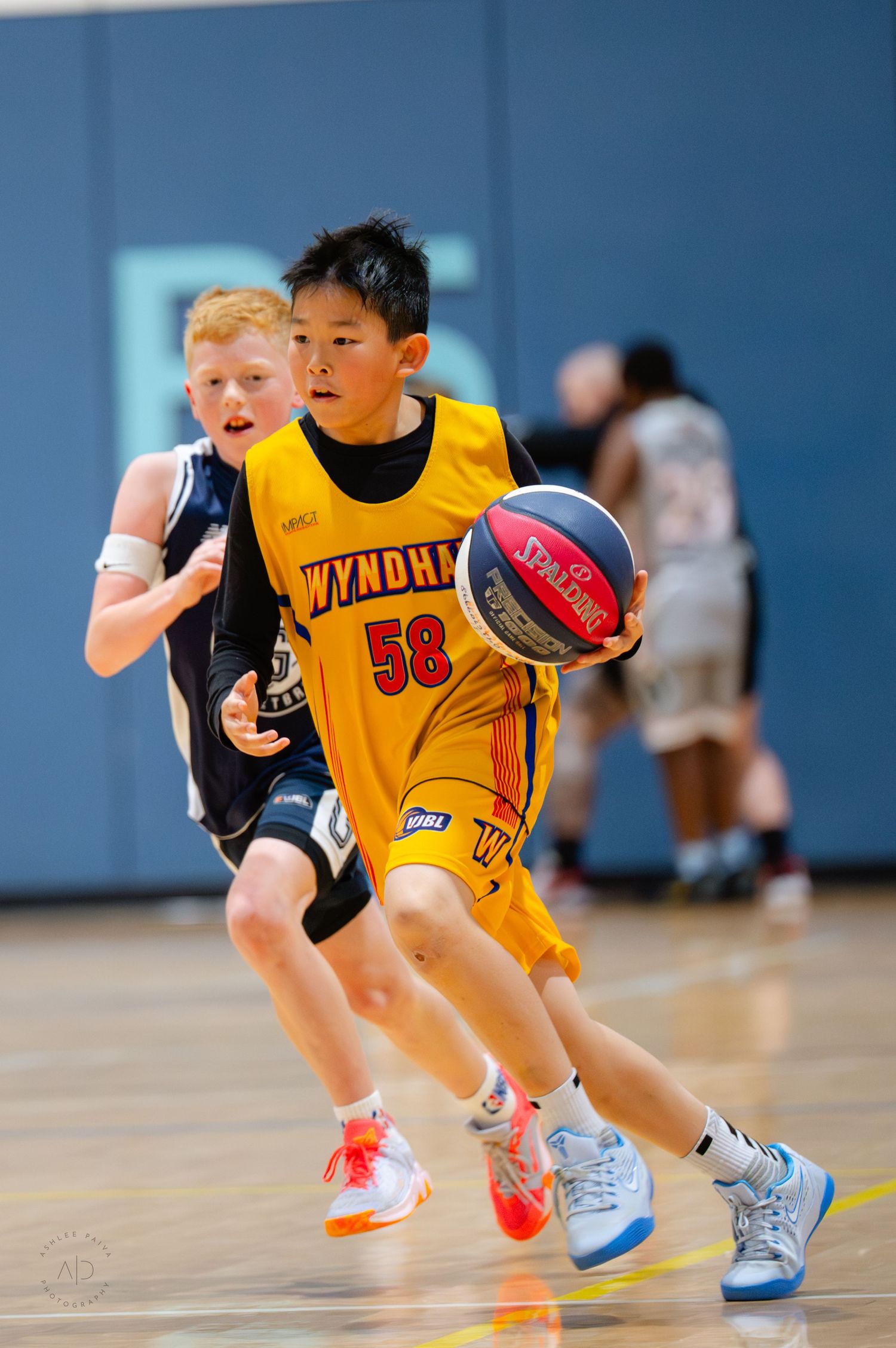 Young basketball player in yellow Wyndham #58 jersey dribbles past defender during indoor youth basketball game.