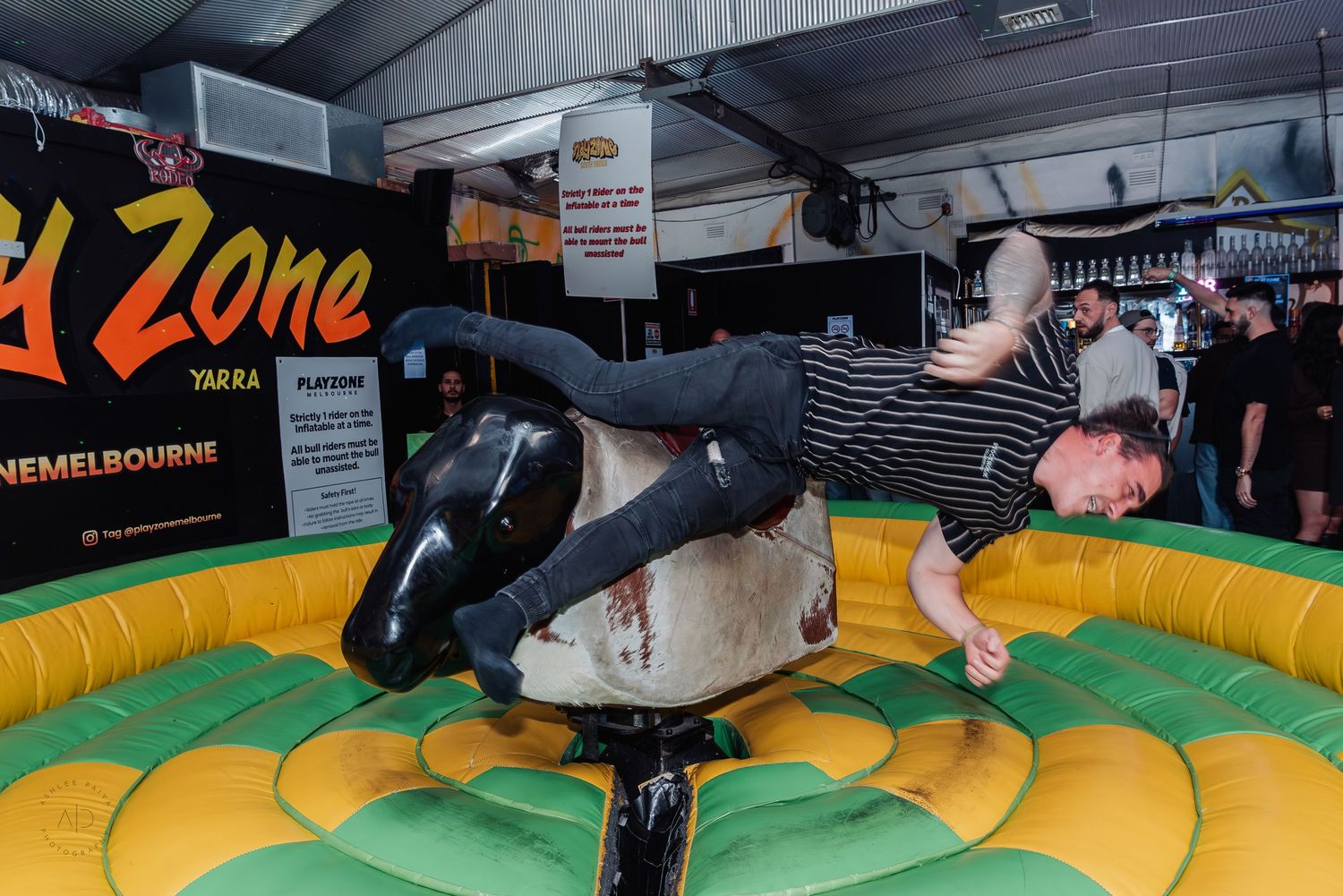 Person riding a mechanical bull at Zone Bar in Melbourne on a yellow inflatable mat.