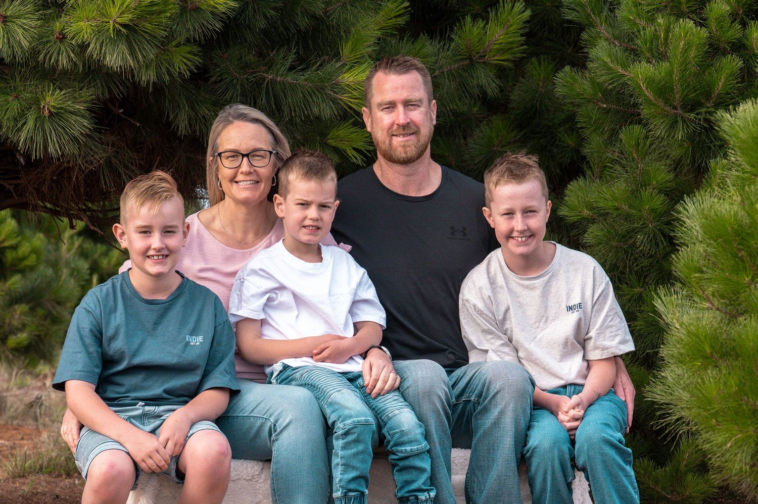 Group portrait against evergreen trees showing casual outdoor family gathering.