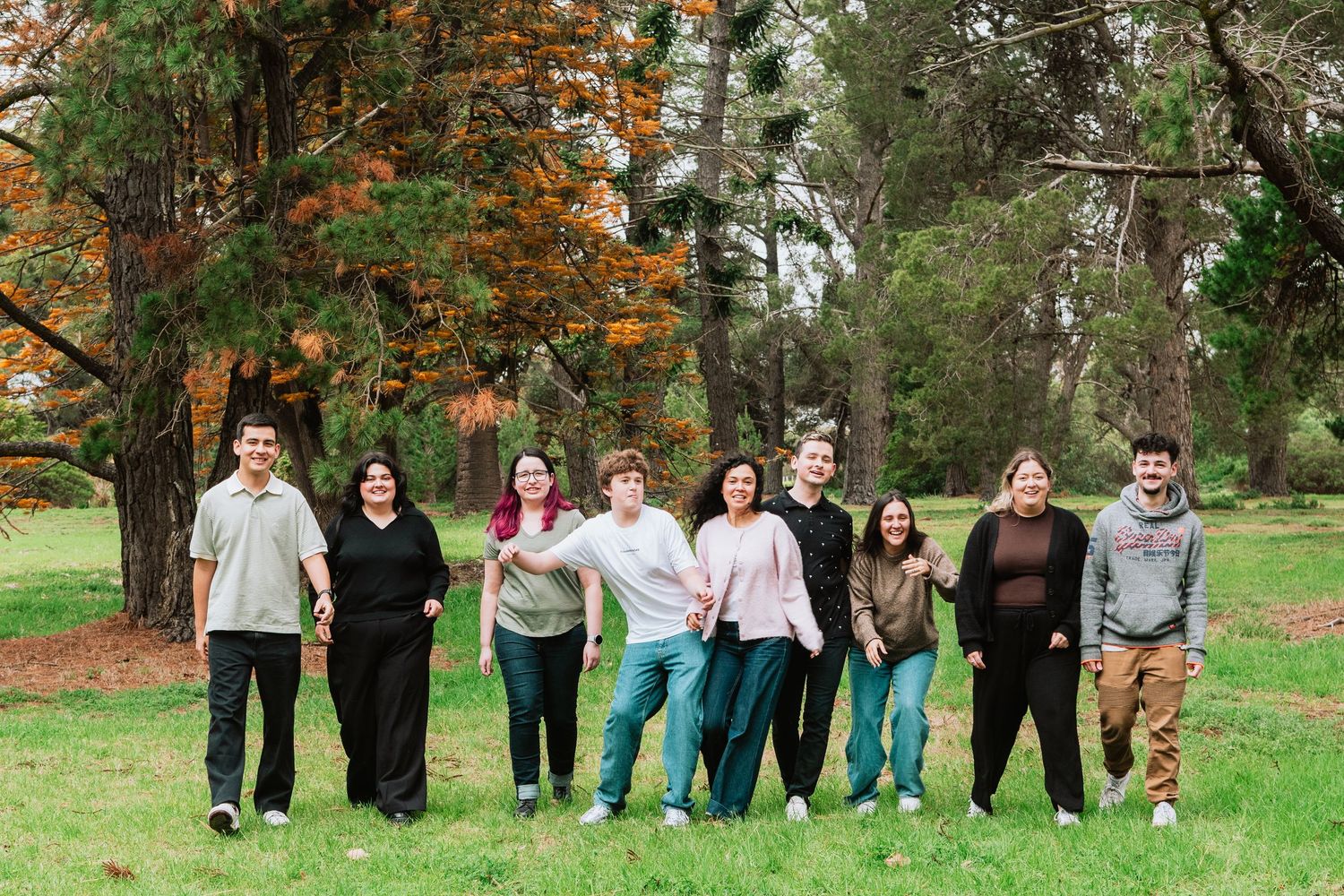 Group photo in a park with autumn trees and green grass in the background.