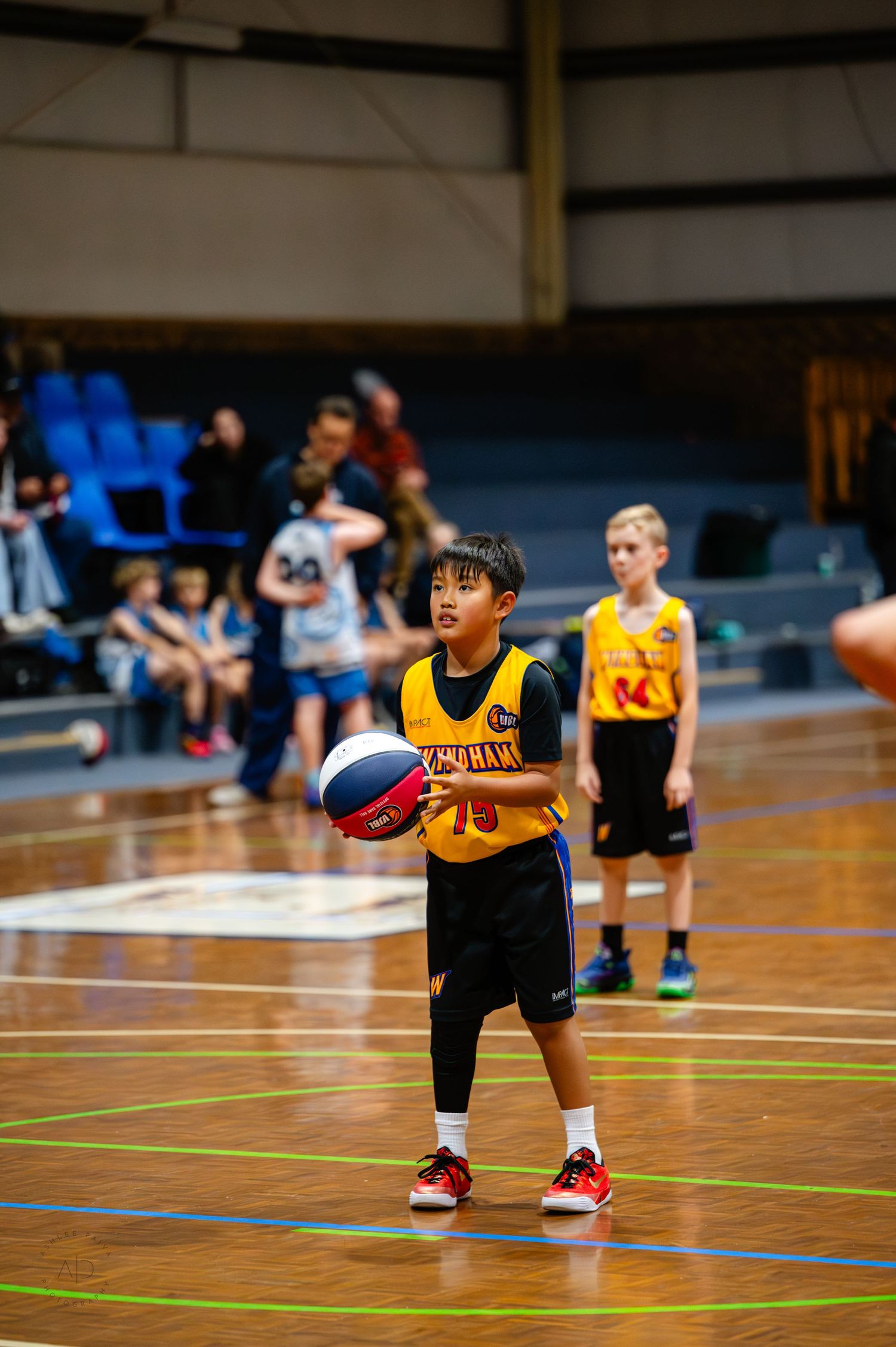 Young boy in yellow basketball jersey holds ball on indoor court during youth basketball game.