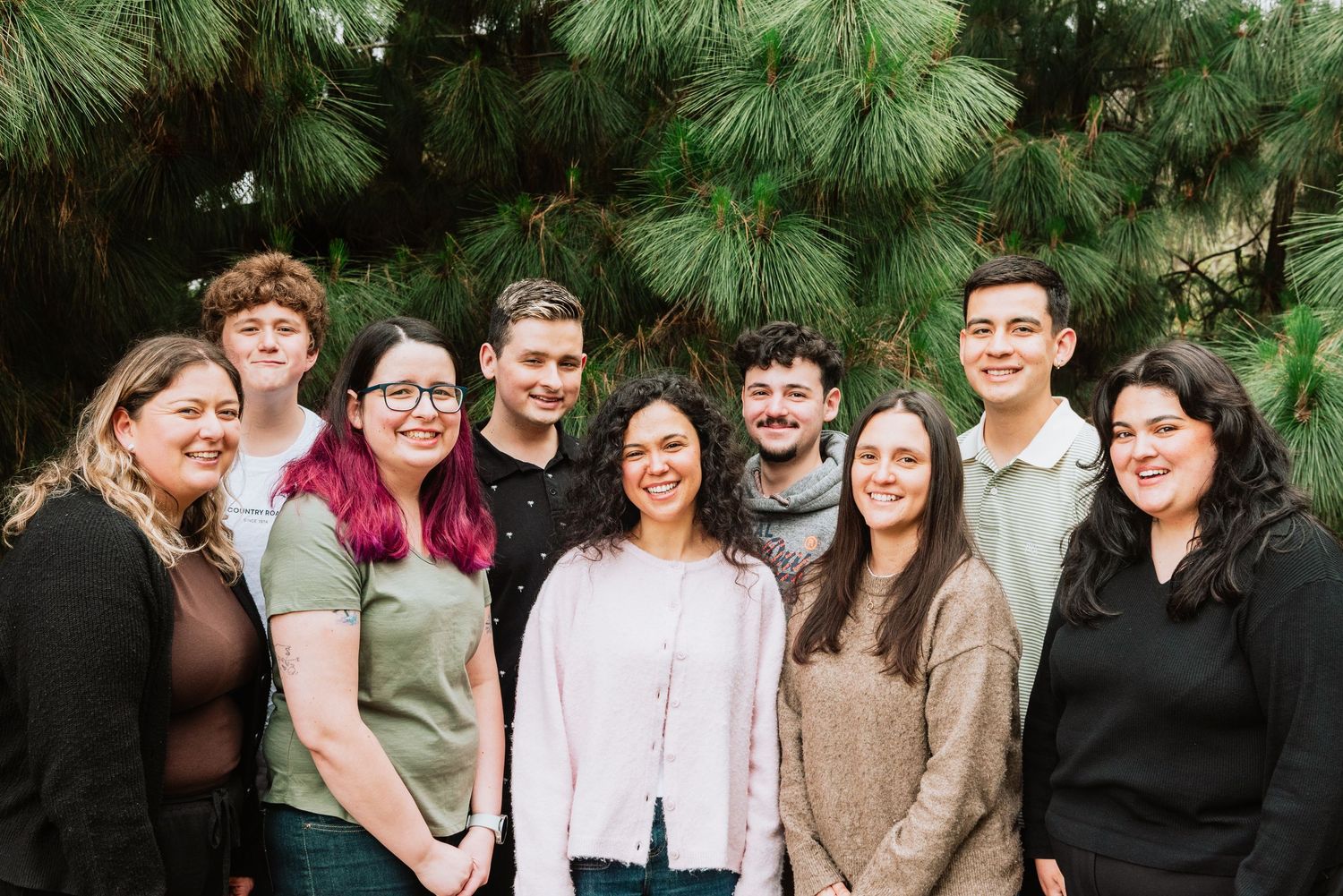 Casual group gathering under pine trees in an outdoor setting.
