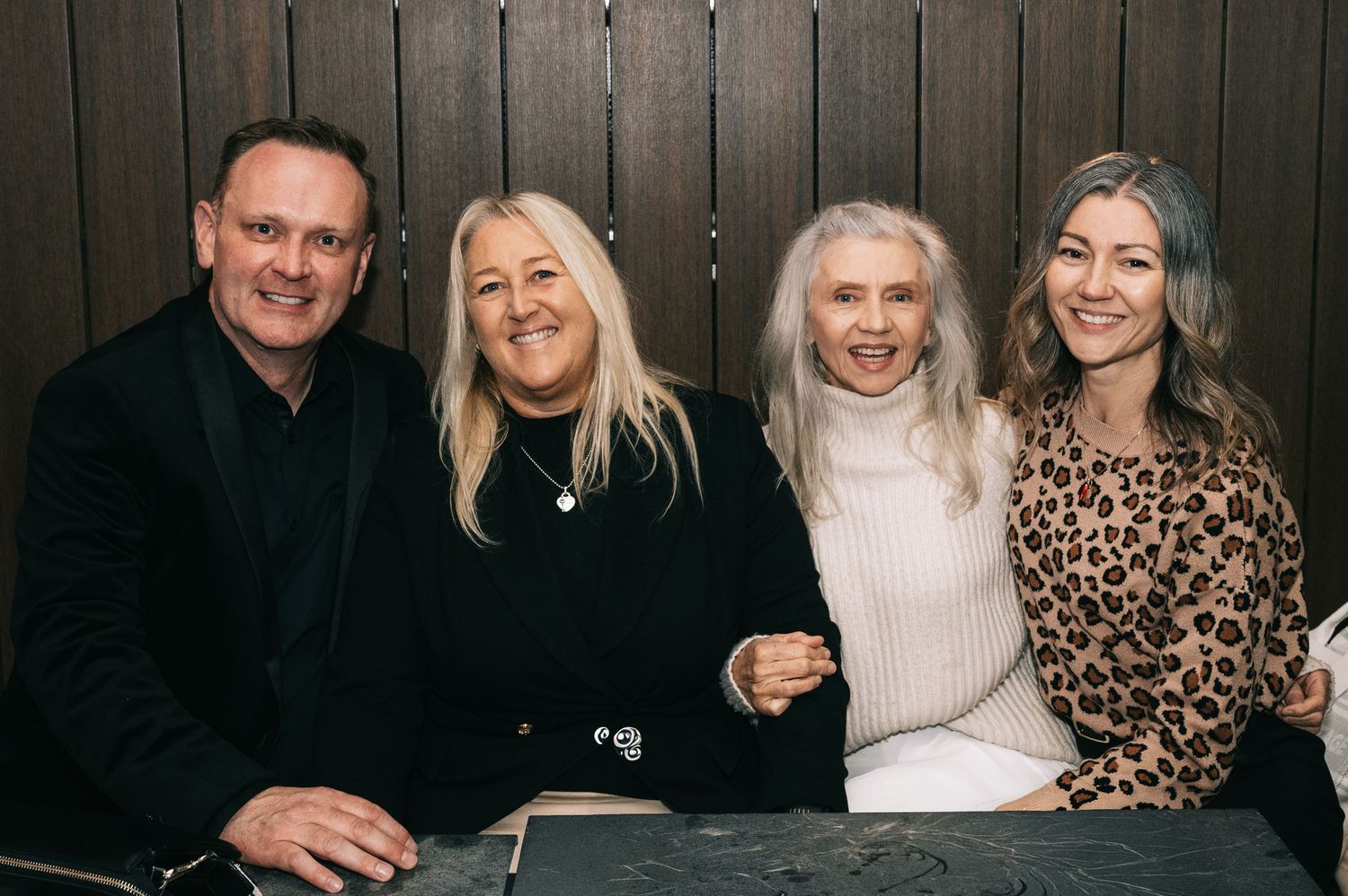 Four people smile while sitting together at a dark wooden table.
