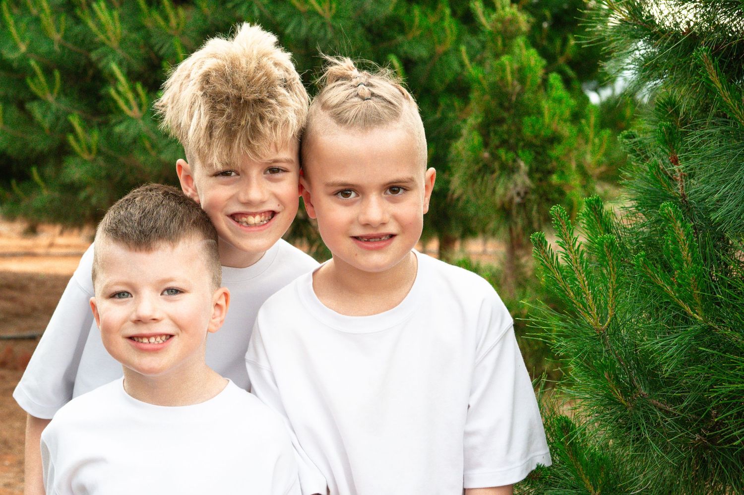 Children smiling and playing between rows of pine trees at a tree farm.