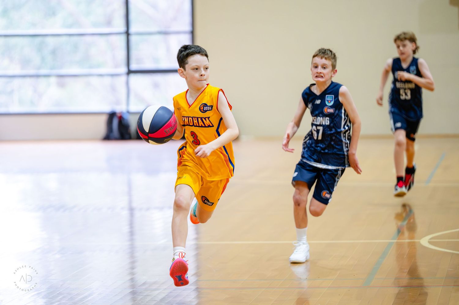 Young boys playing youth basketball game indoors, player in yellow dribbling ball down court.