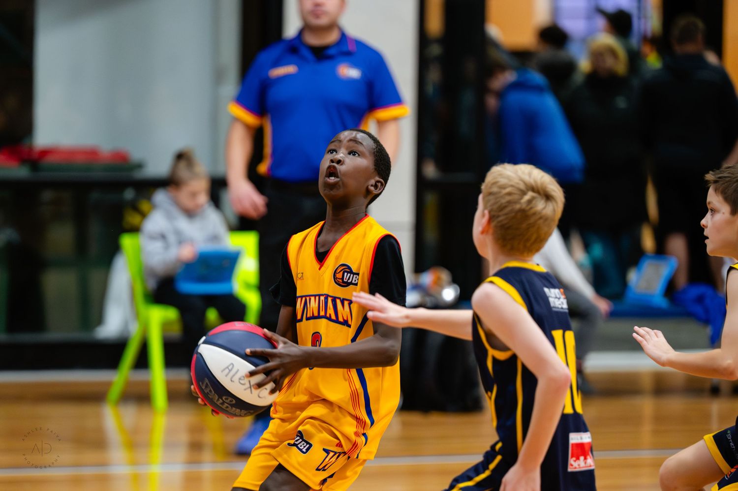 Young basketball players compete in an indoor youth game, with a player in yellow dribbling toward the basket.
