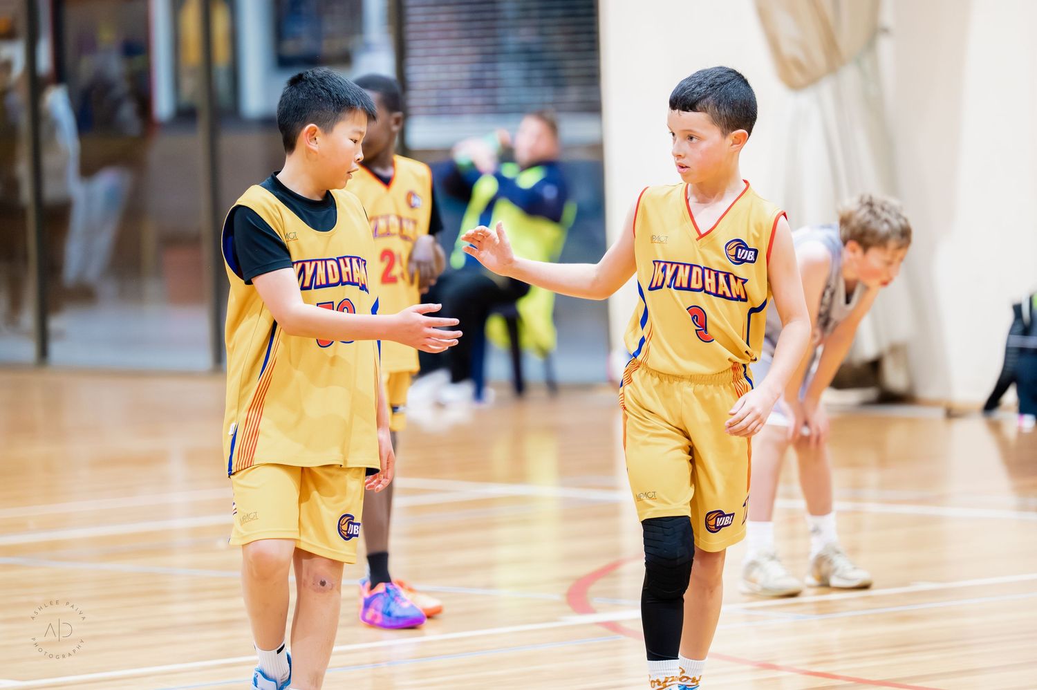 Two young boys in yellow Bulldogs basketball uniforms high-fiving during a youth basketball game indoors.