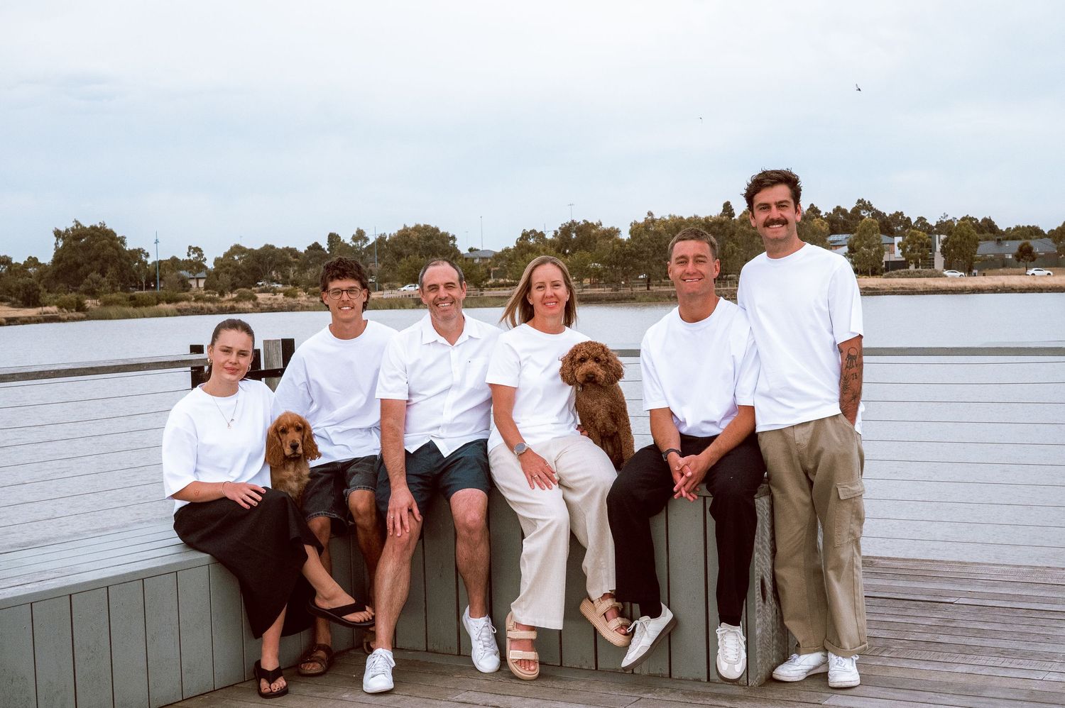 A group sits casually together on a wooden deck overlooking the water.