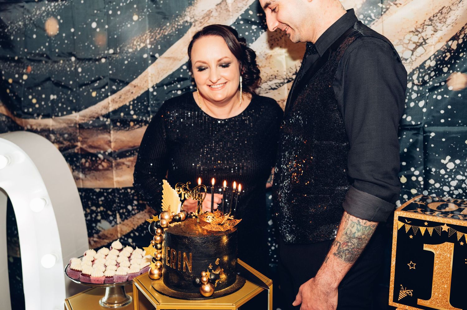Couple admiring a birthday cake decorated with candles at a celebration.