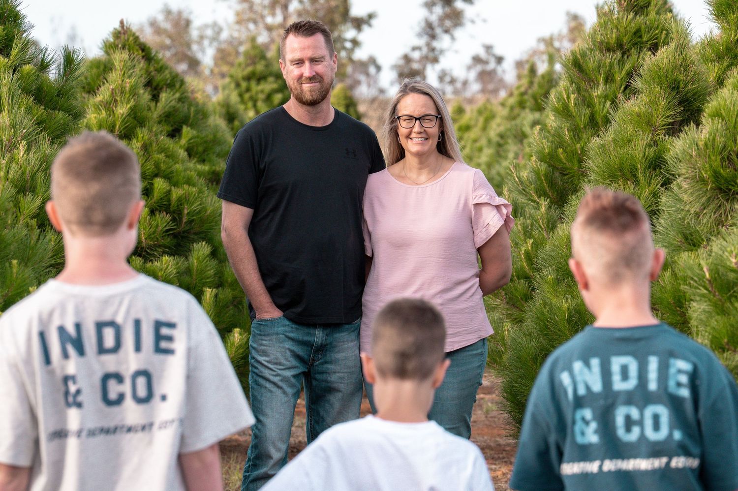 Family walking together through pine trees wearing casual clothing.