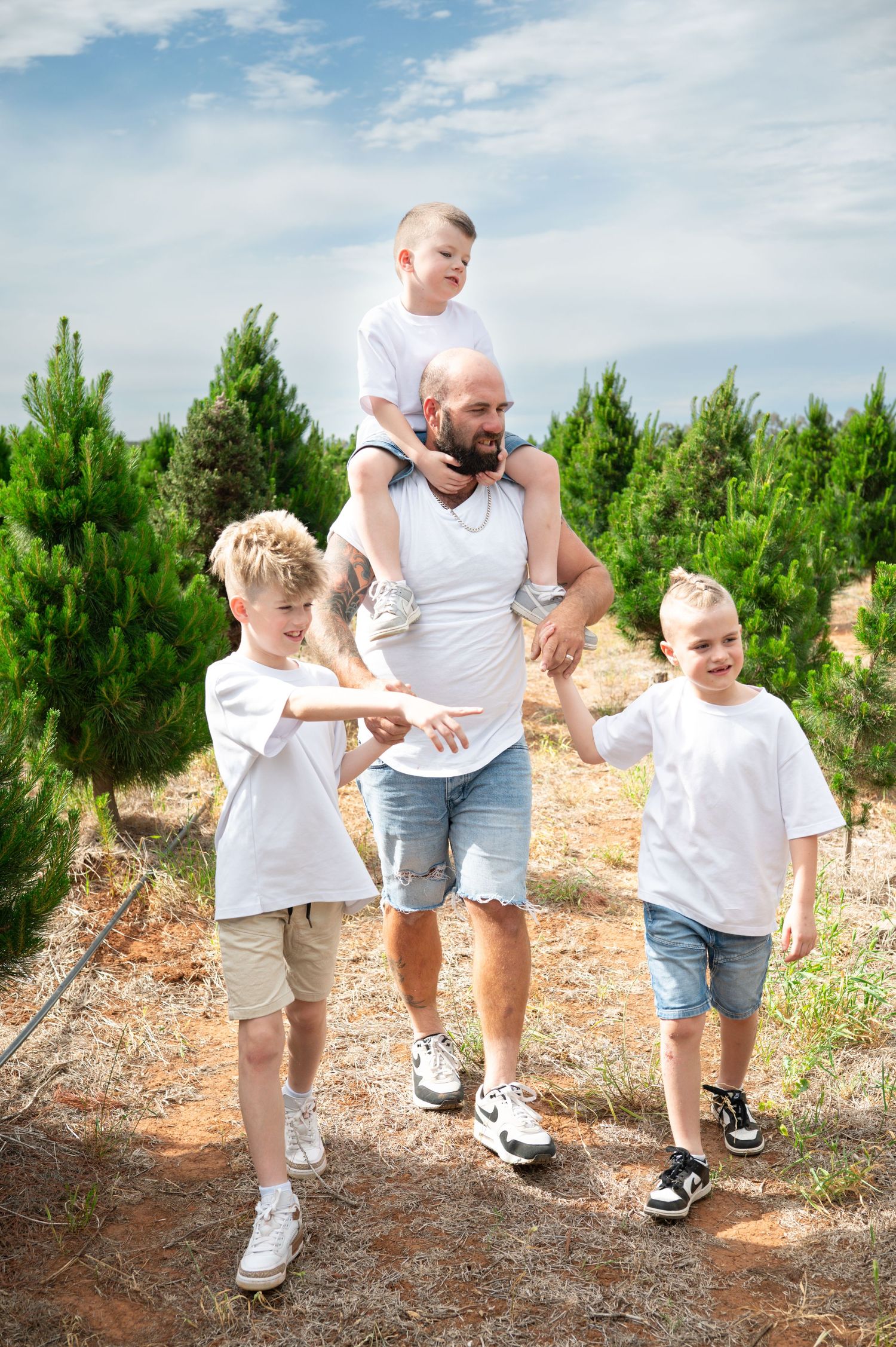 Family walking together on a red dirt path through a pine tree farm.