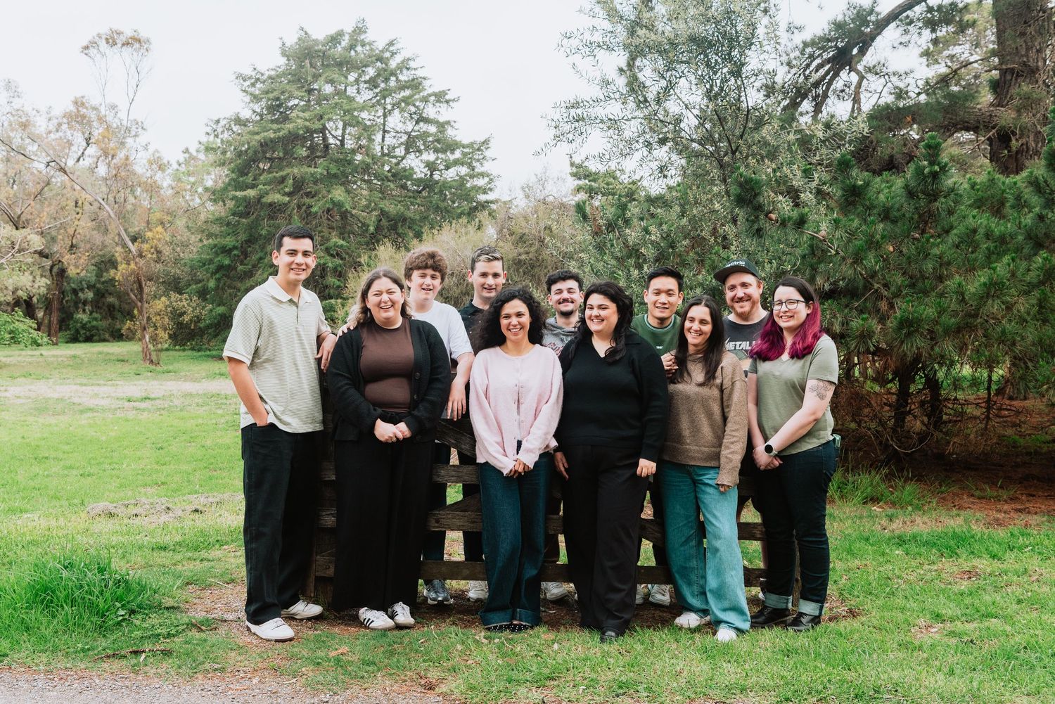 Wide group shot of people gathered outdoors with trees and grass in the background.