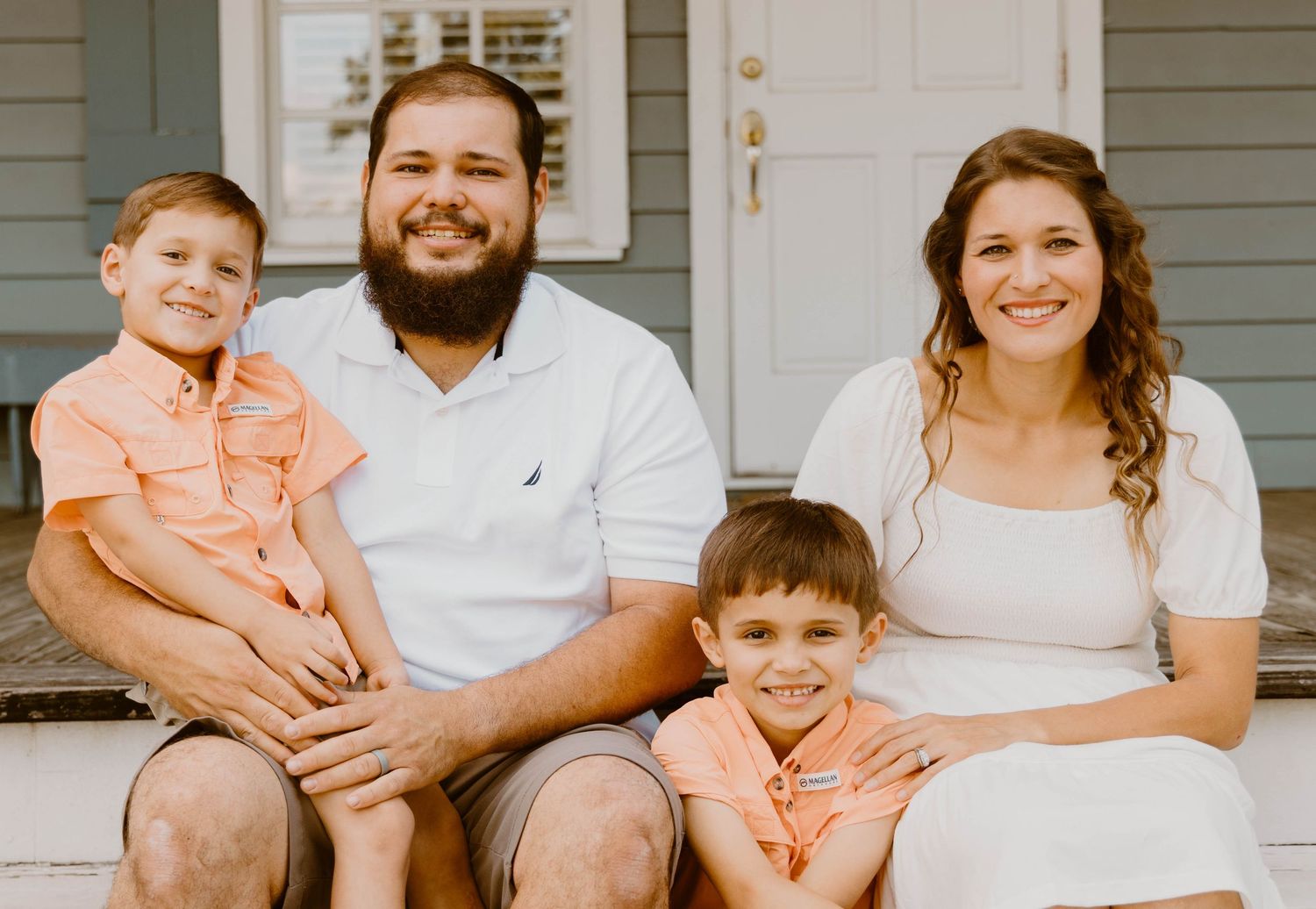 Casual family portrait on white wooden porch steps of gray house.