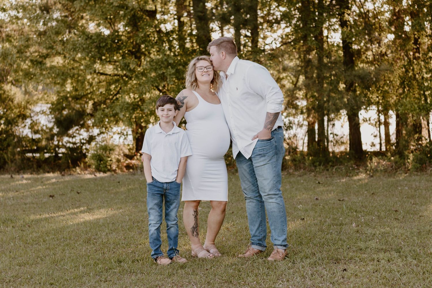 Casual outdoor family photo with white dress and jeans in natural setting.