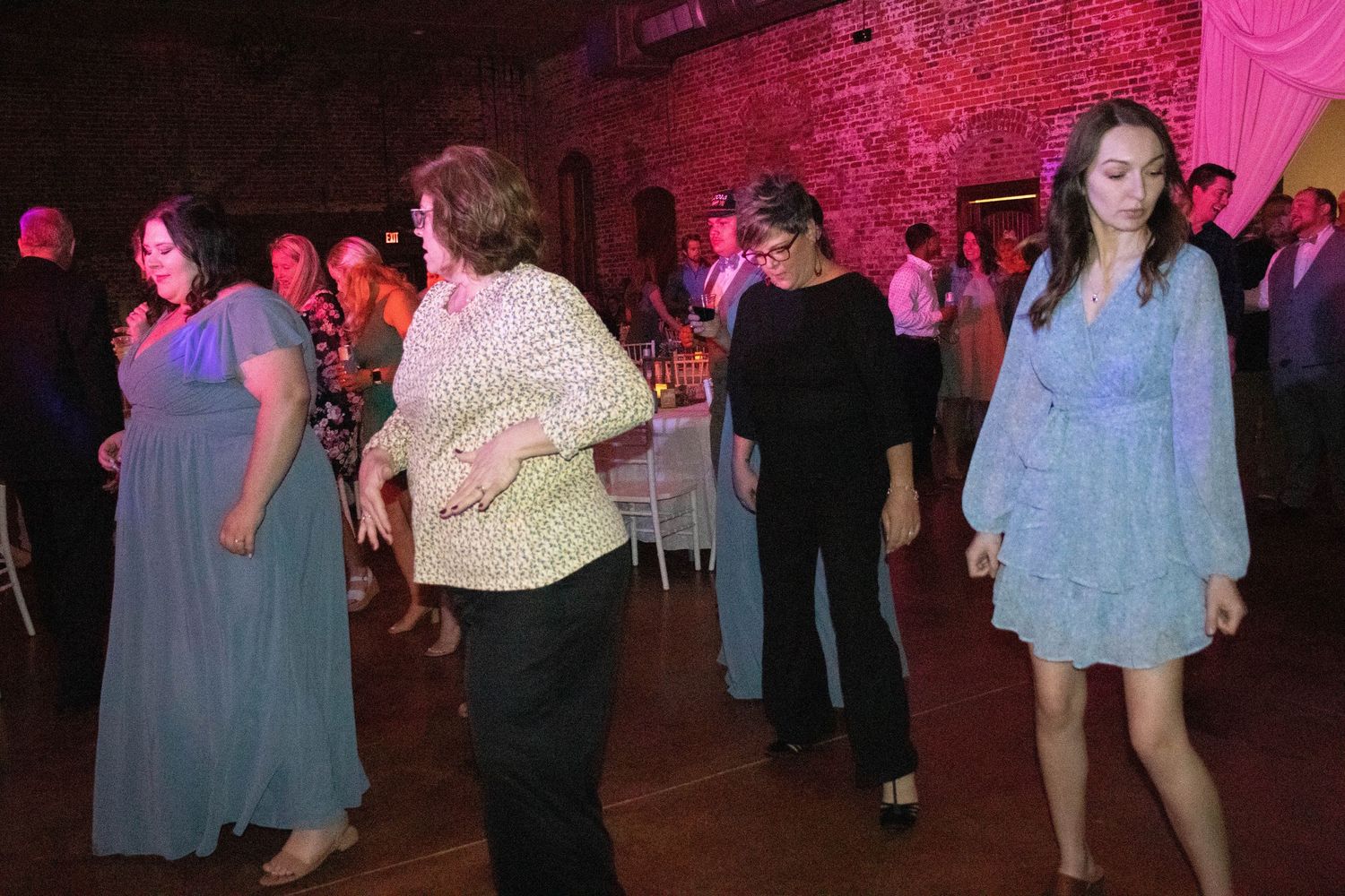 Party guests dance under pink mood lighting in a brick-walled event space.