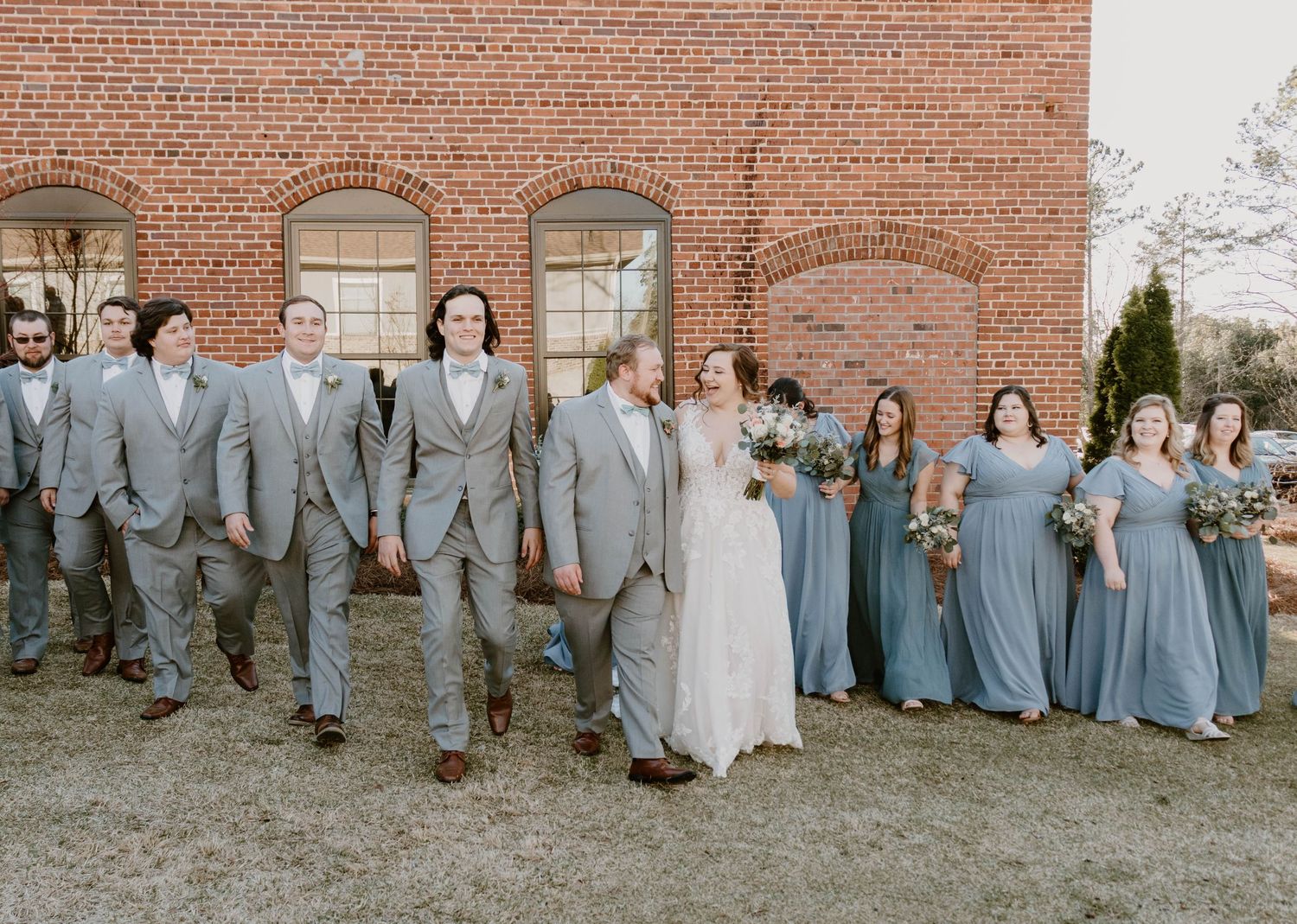 Bridal party lineup against rustic brick building in grey and blue color scheme.