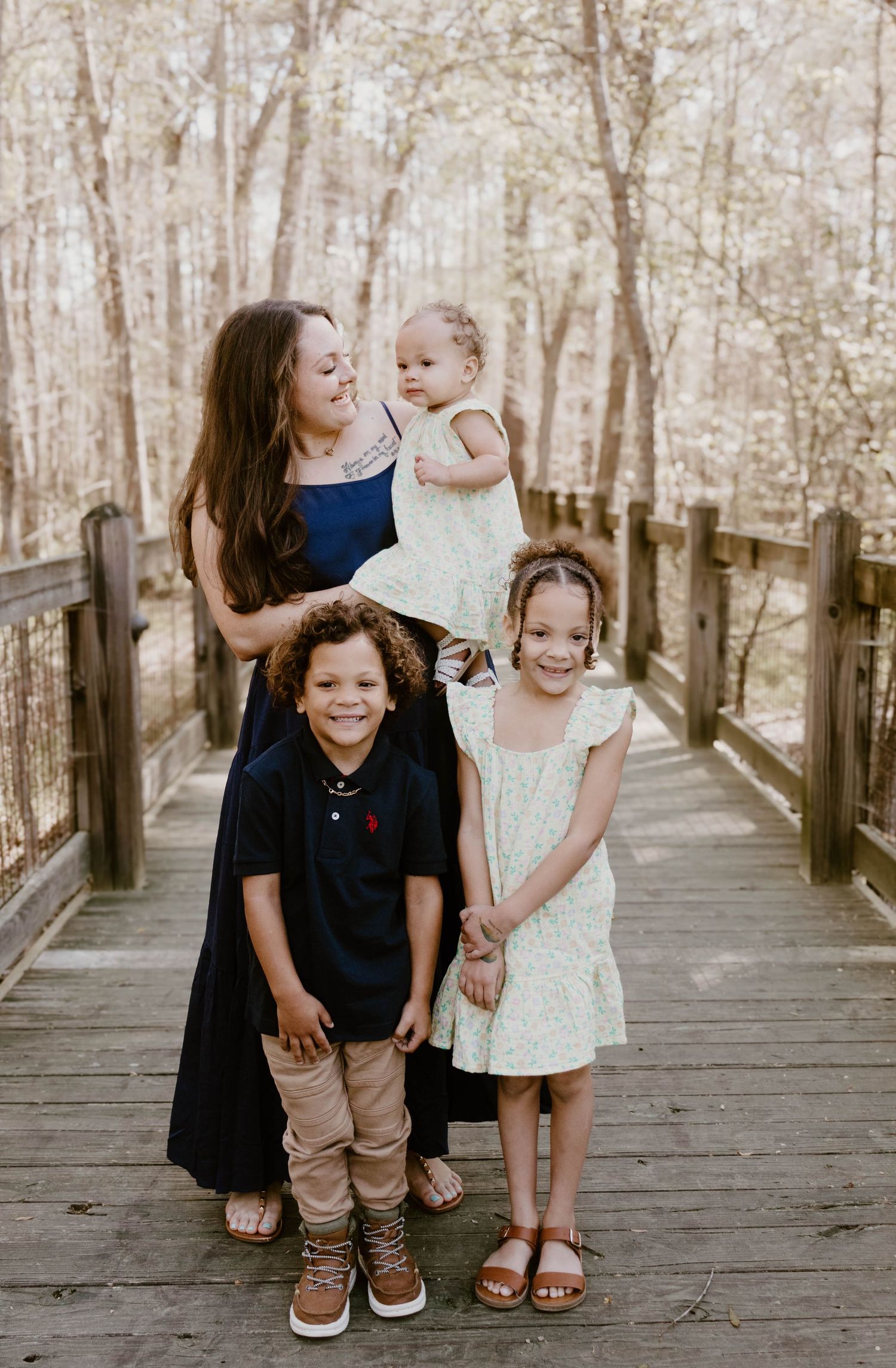 A family of four poses together on a wooden walkway in the woods during a photo session.