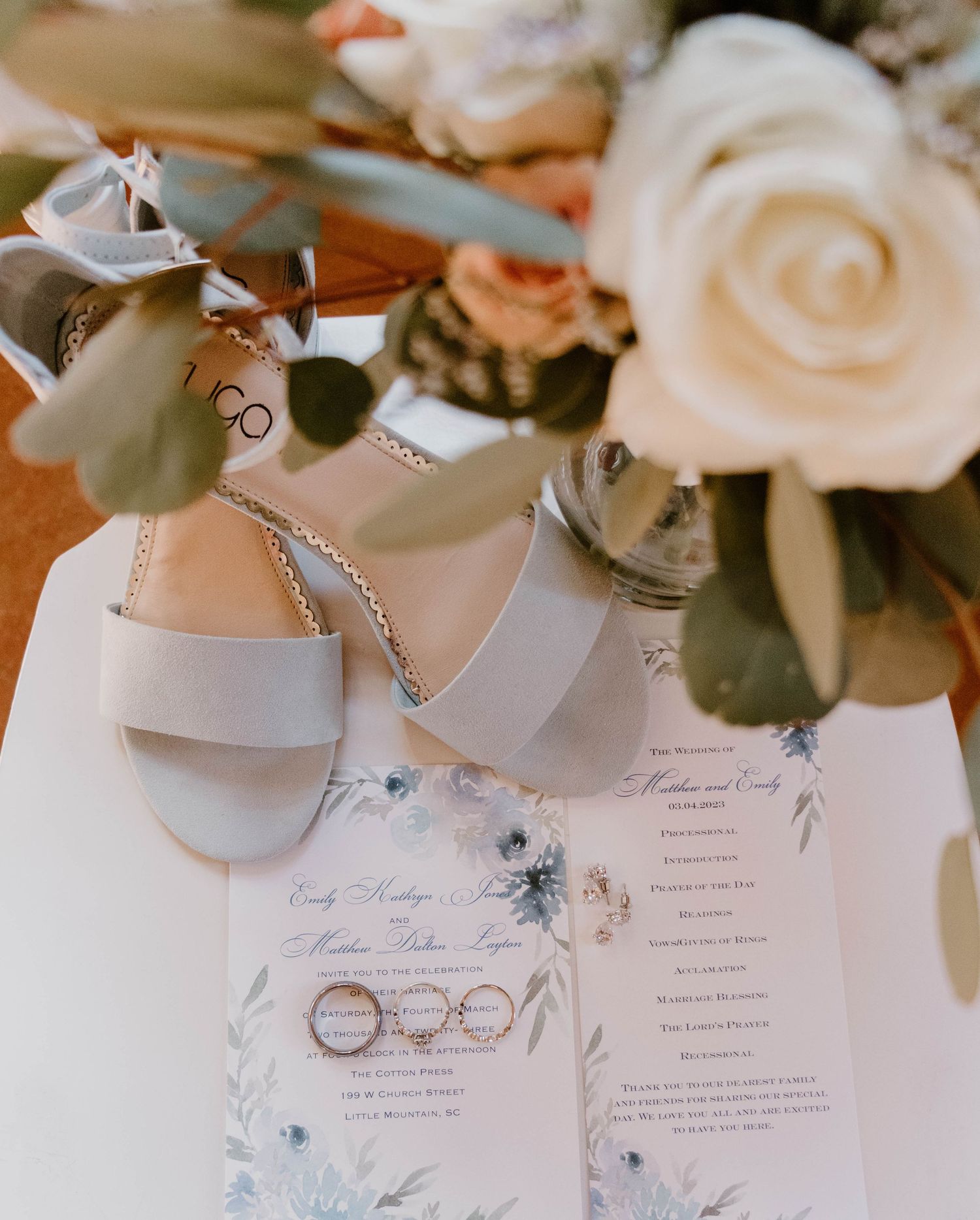 Wedding details including white roses, rings, and invitation cards with blue floral designs.