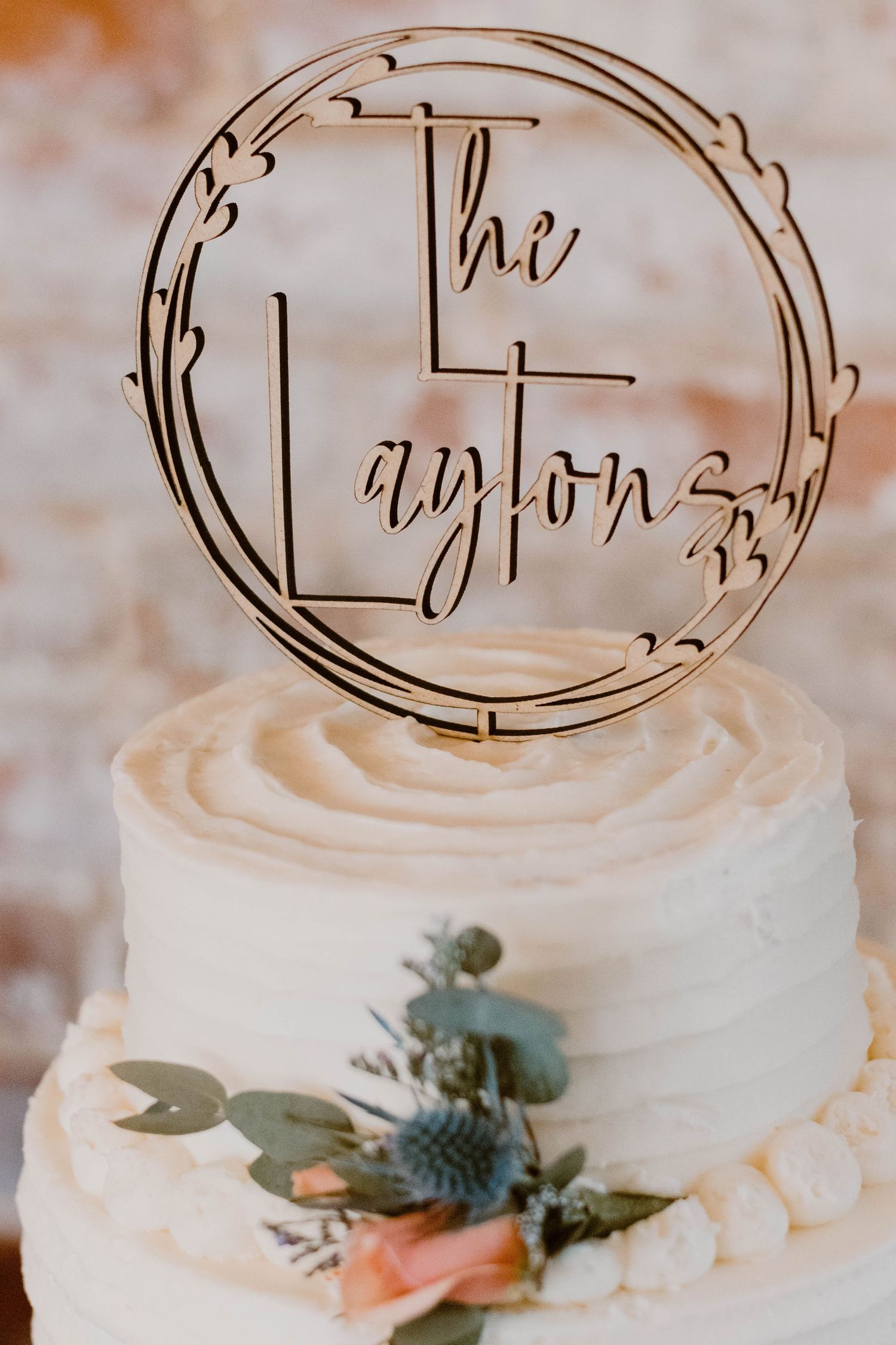 Close-up of white wedding cake tiers with metallic monogram topper and floral accents.