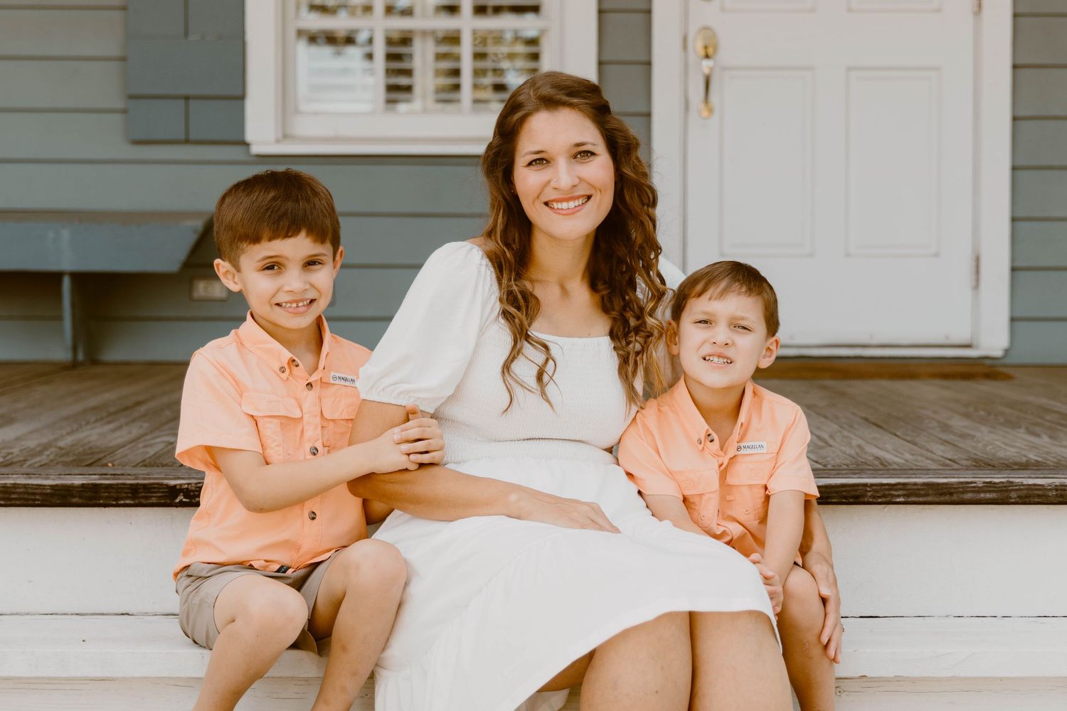 Family group photo on weathered white porch steps with gray siding backdrop.
