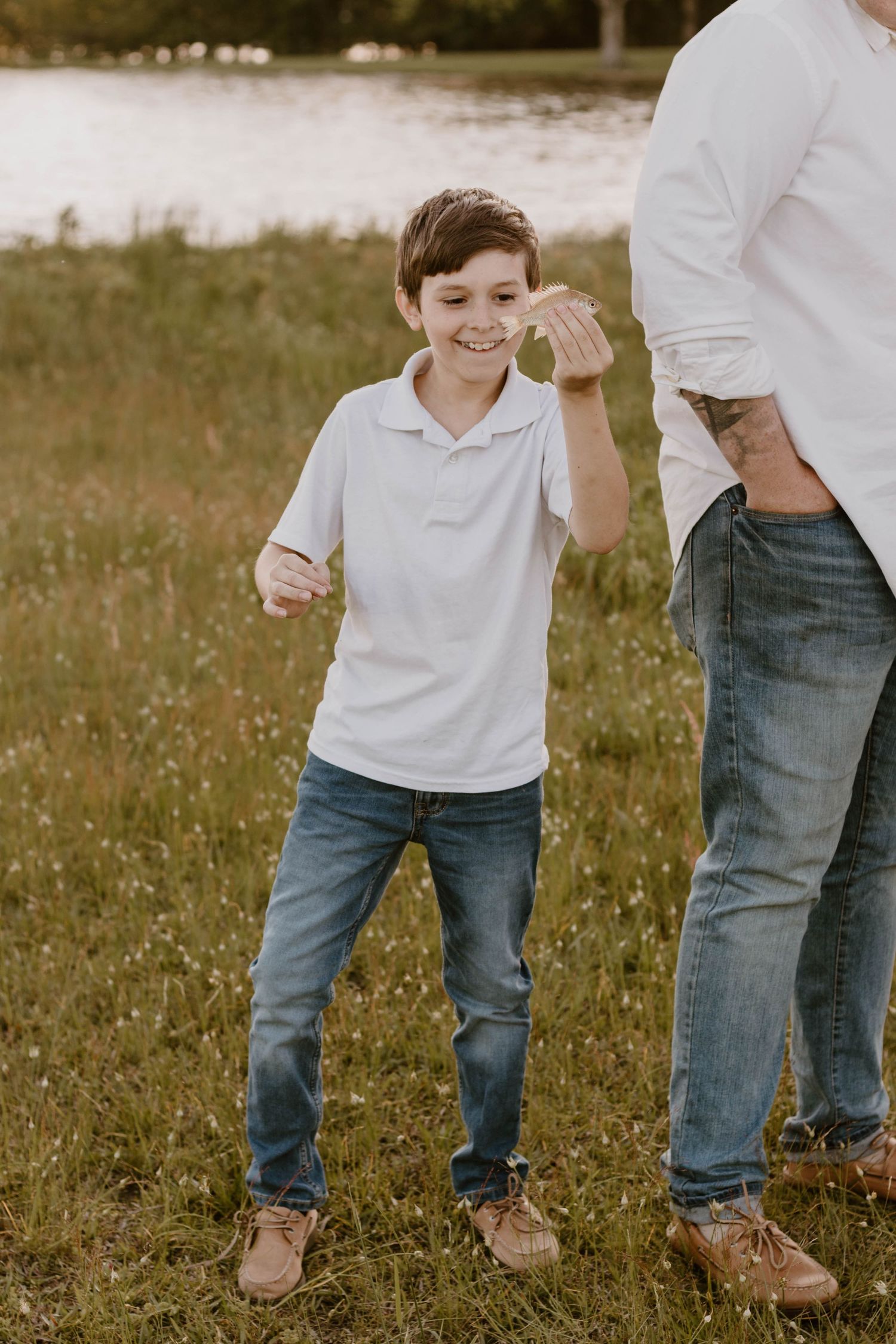 A young boy in a white polo shirt smiles joyfully while playing outdoors.