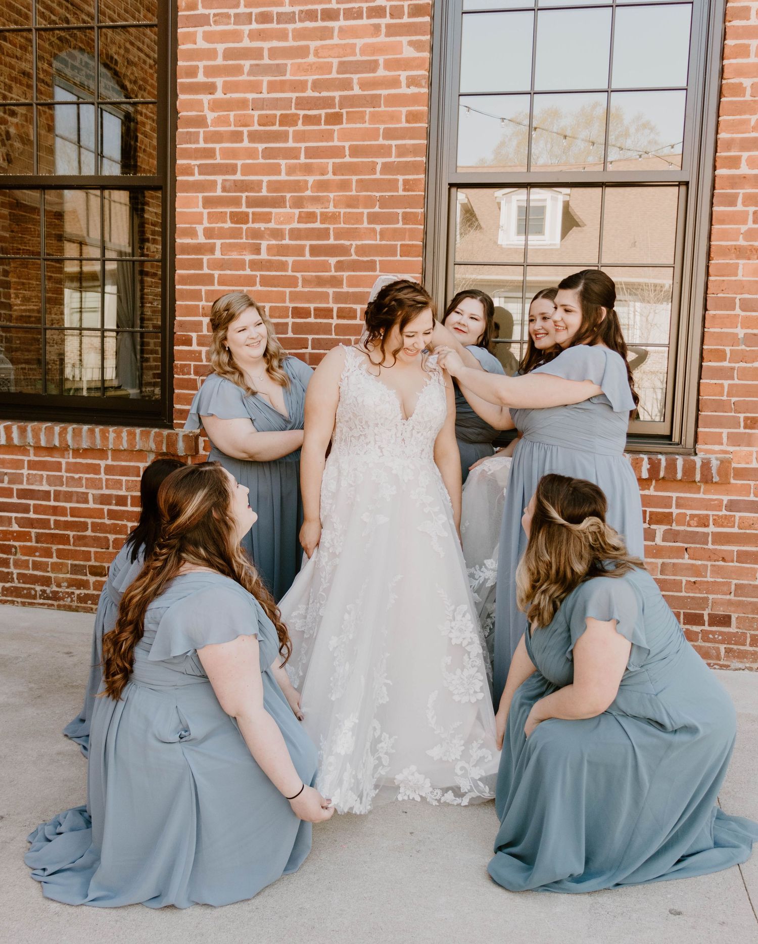 Candid moment of bridal party in blue dresses sitting together on brick steps.