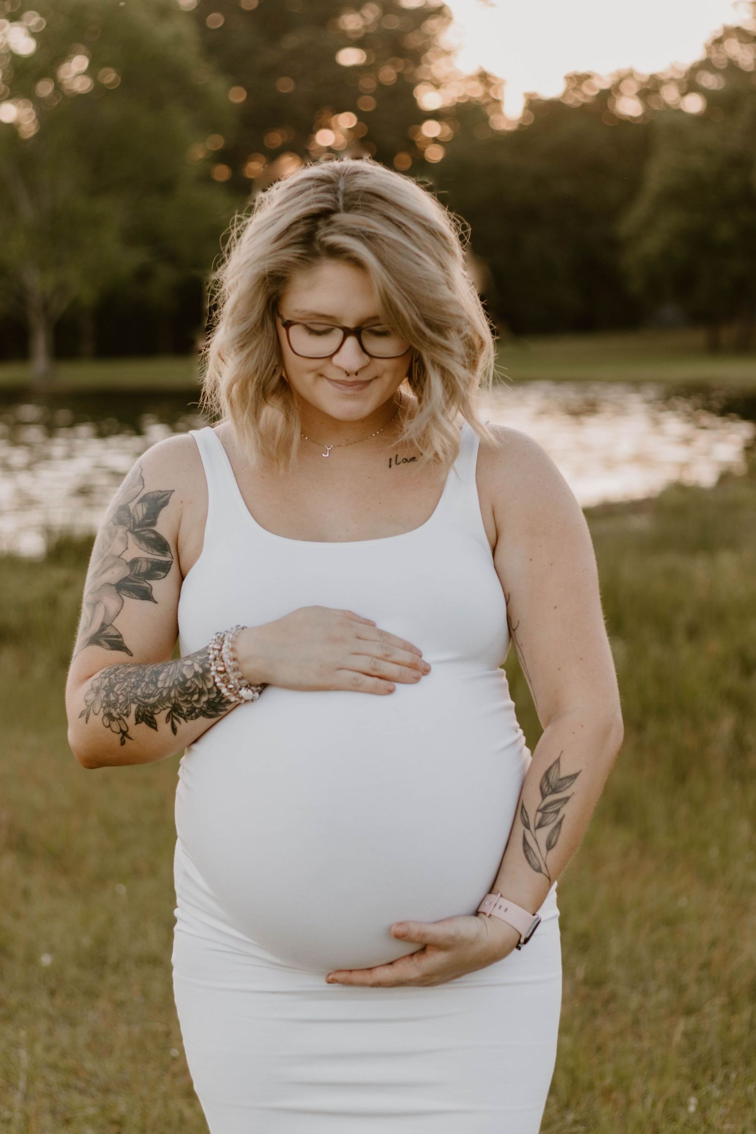 Artistic maternity portraits showing tattoos and baby bump against sunset.