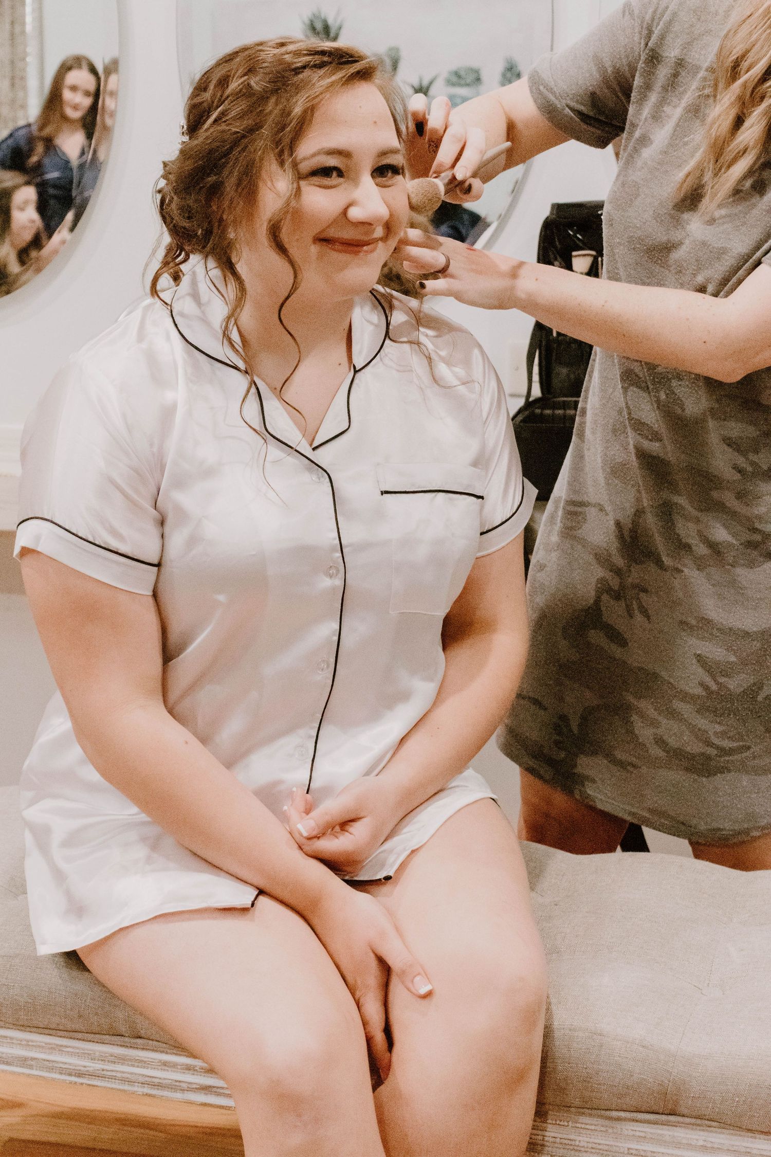 Bride in white robe gets ready with hair and makeup before the wedding.