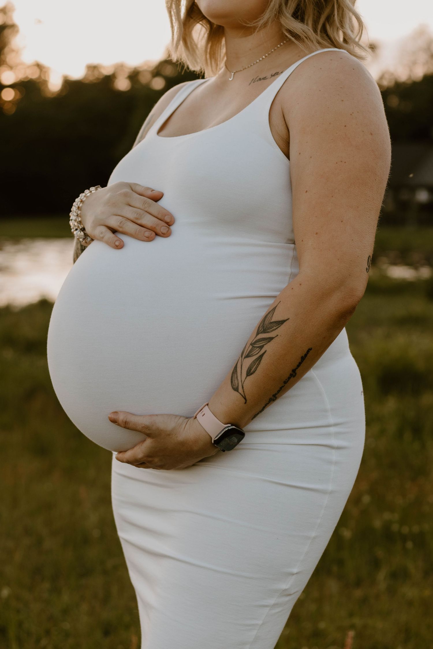 Maternity portraits in white dress against golden hour lighting.
