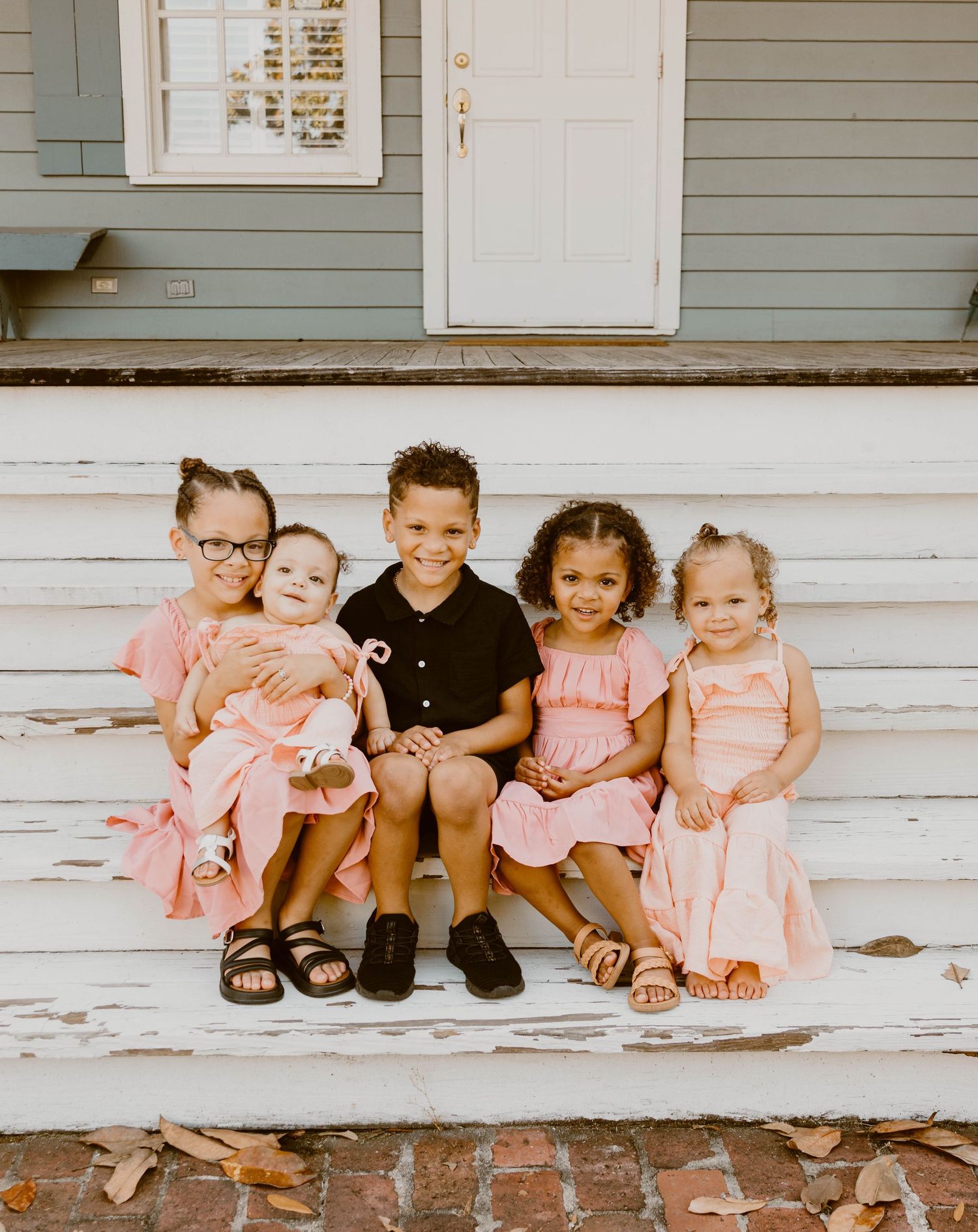Five children sit together on white wooden steps wearing coordinated pink and black outfits.