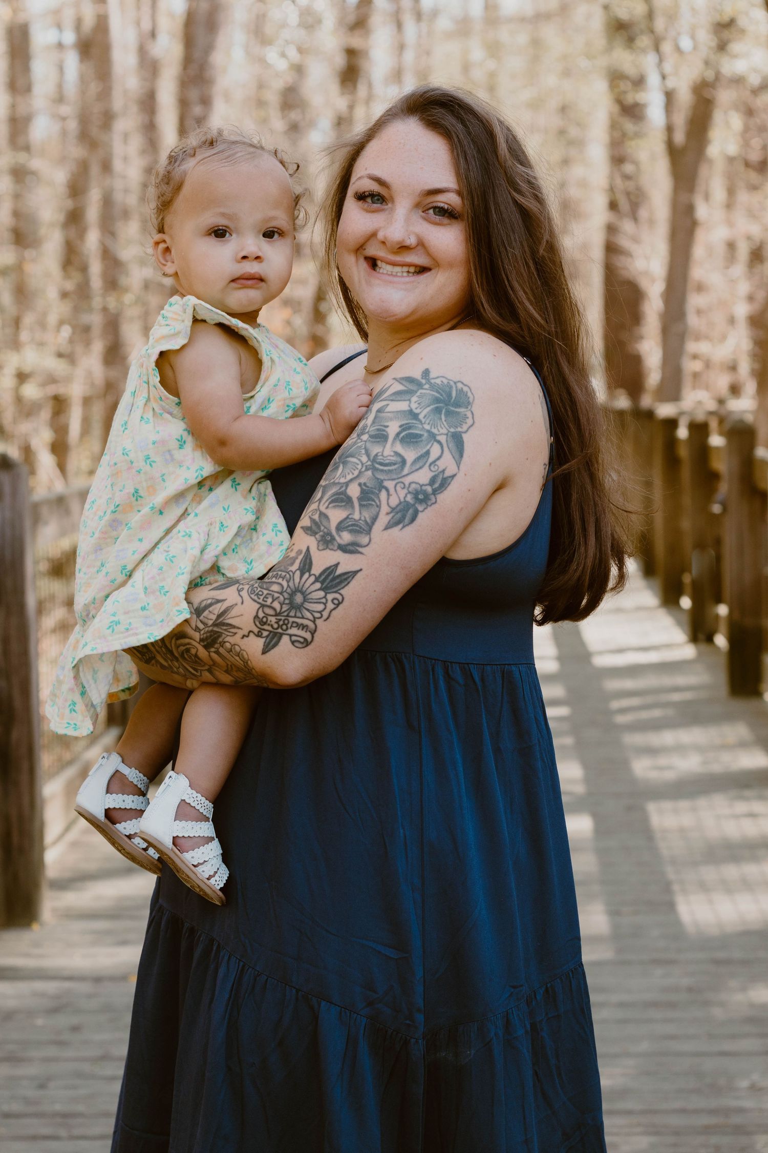 Mother and child sharing an embrace while wearing matching navy blue dresses on a wooden walkway.