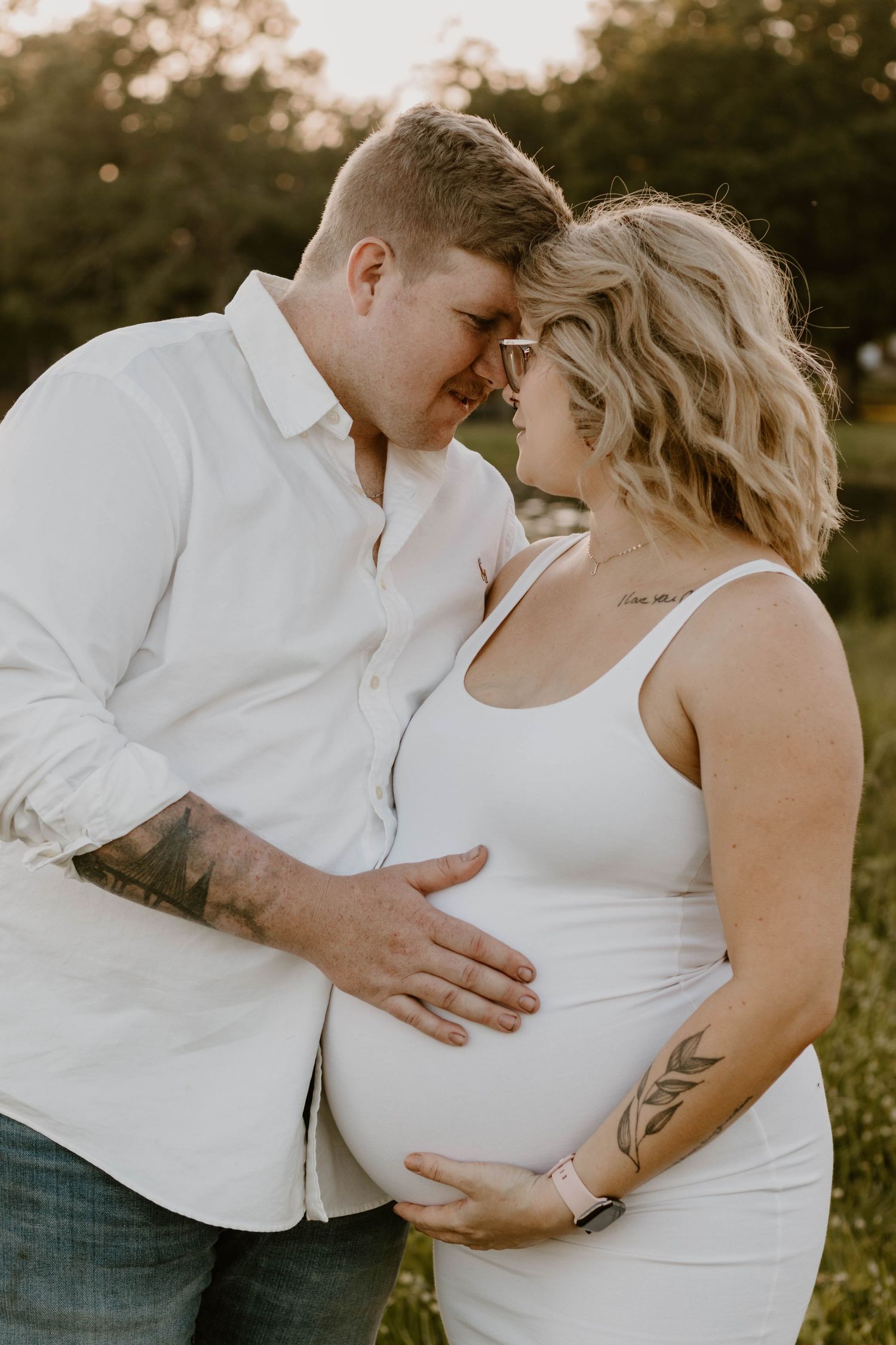 An intimate moment between a couple as they touch foreheads and cradle her pregnant belly.